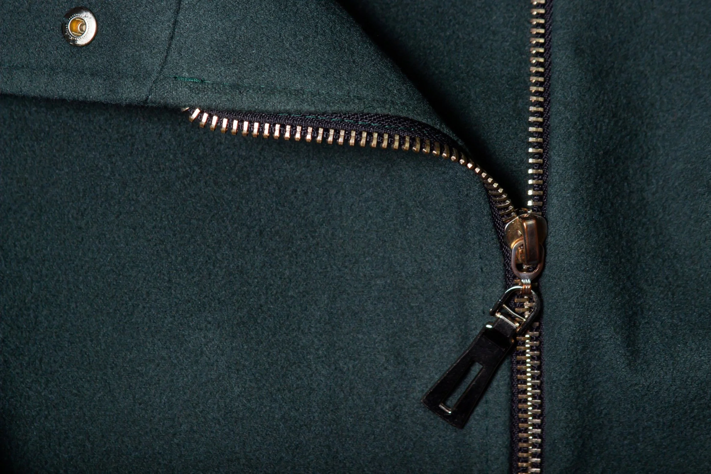 Close-up of a dark green jacket with a partially unzipped metallic zipper.
