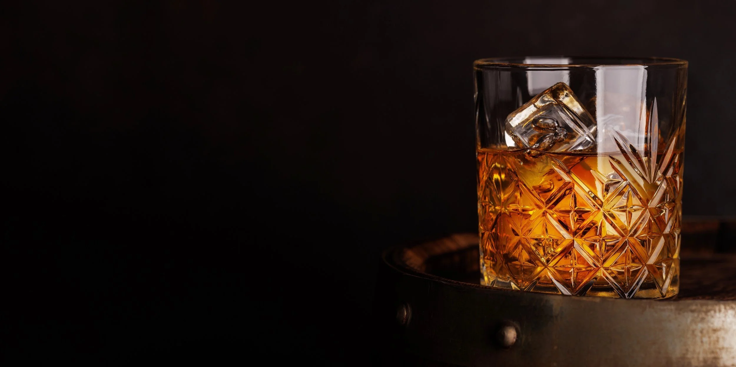A glass of whiskey with ice cubes on a dark surface