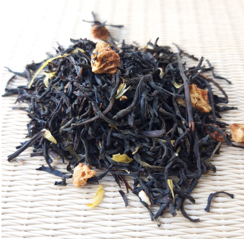 Dry loose black tea leaves with small pieces of dried fruit or flower petals on a woven surface.