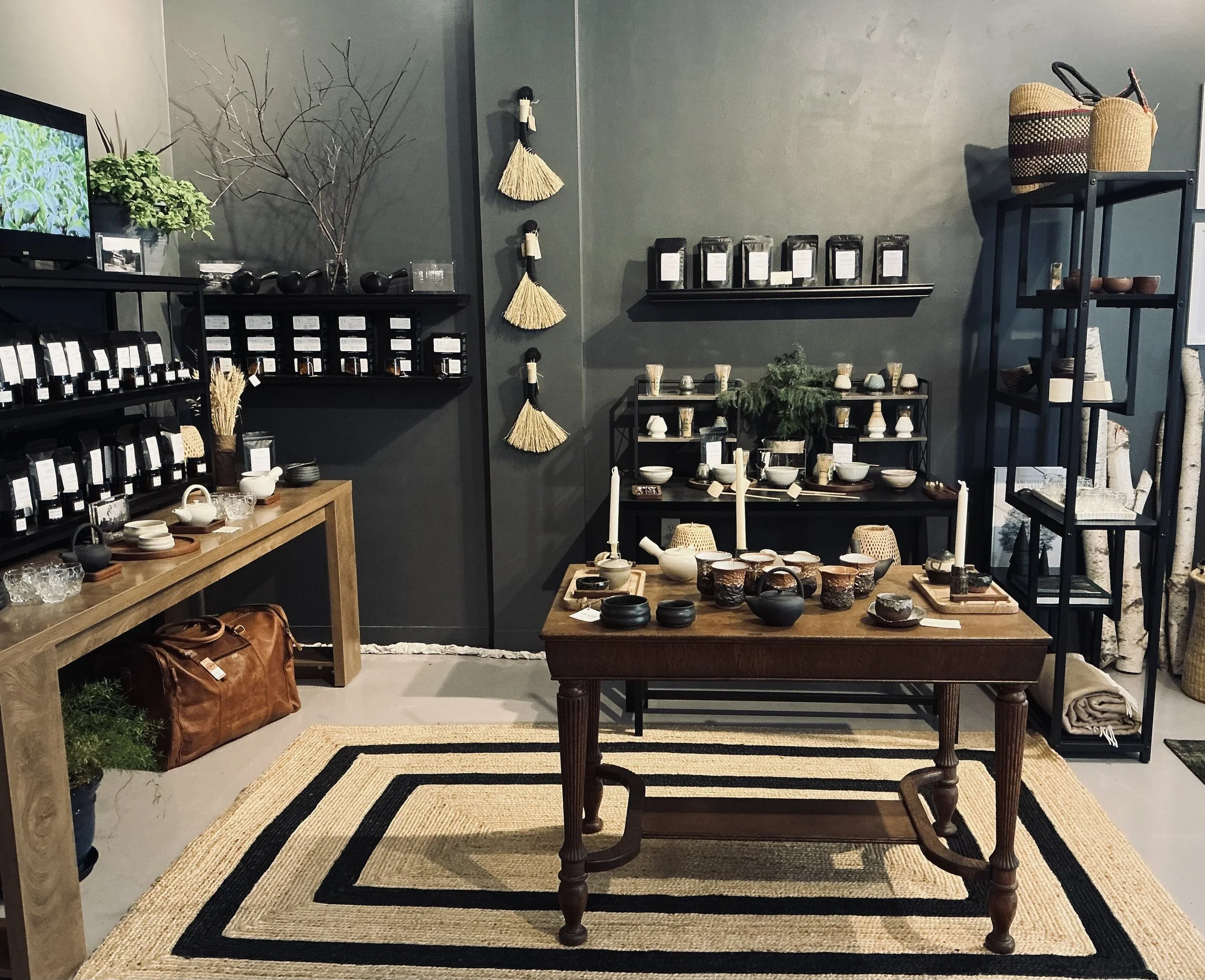 Decorative home goods and ceramics displayed on black and wood shelves and tables, with woven baskets and straw accents, in a modern retail store.