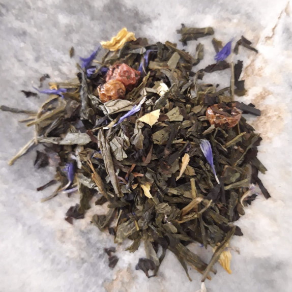 Loose herbal tea with dried leaves, flower petals, and small fruit pieces on parchment paper