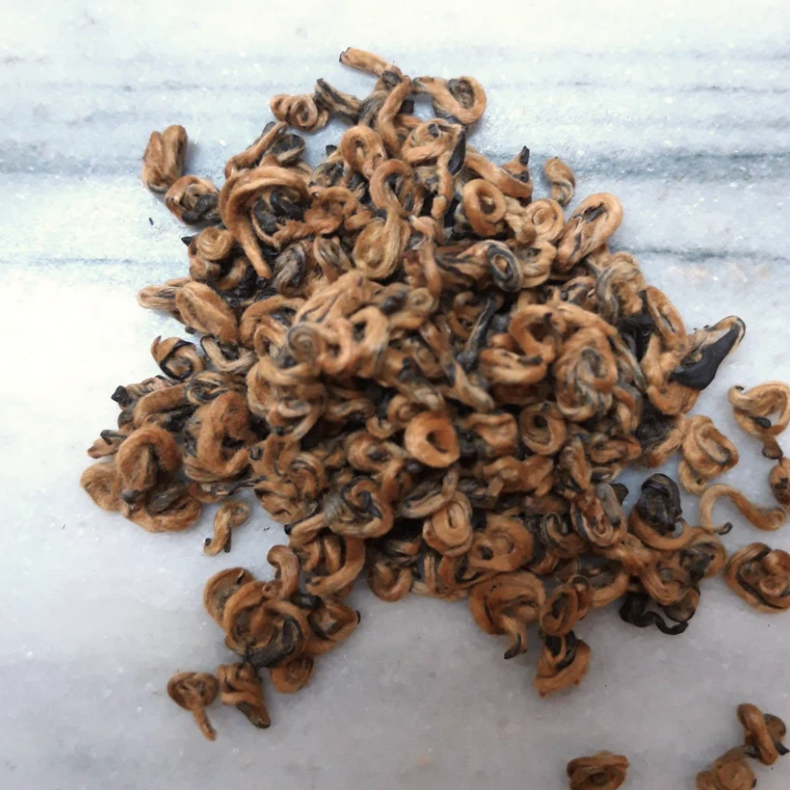 Dried curled pieces of a dark-colored bark or fruit peel on a gray surface.