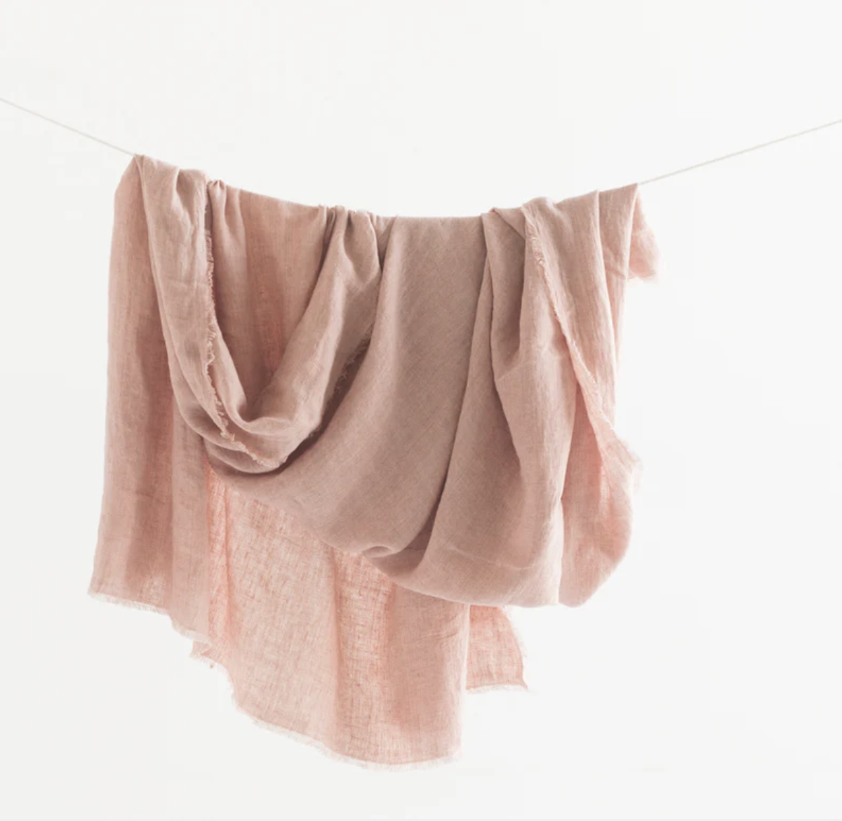Light pink and blush-colored scarves hanging on a clothesline against a white background.
