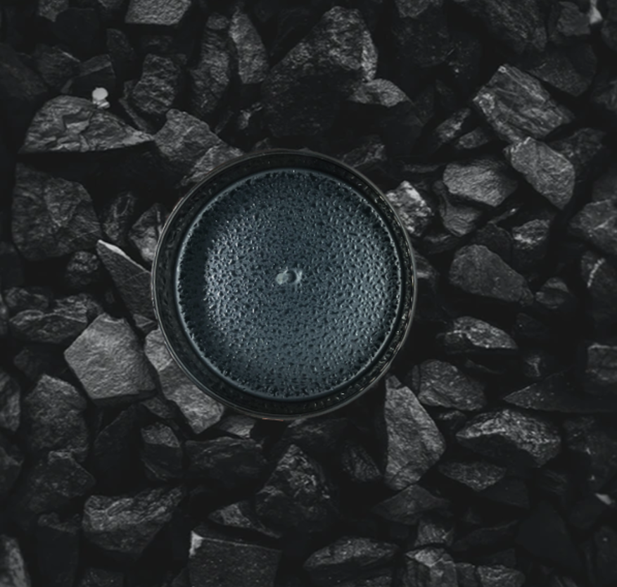 A black cup filled with a dark beverage, resting on black gravel stones.