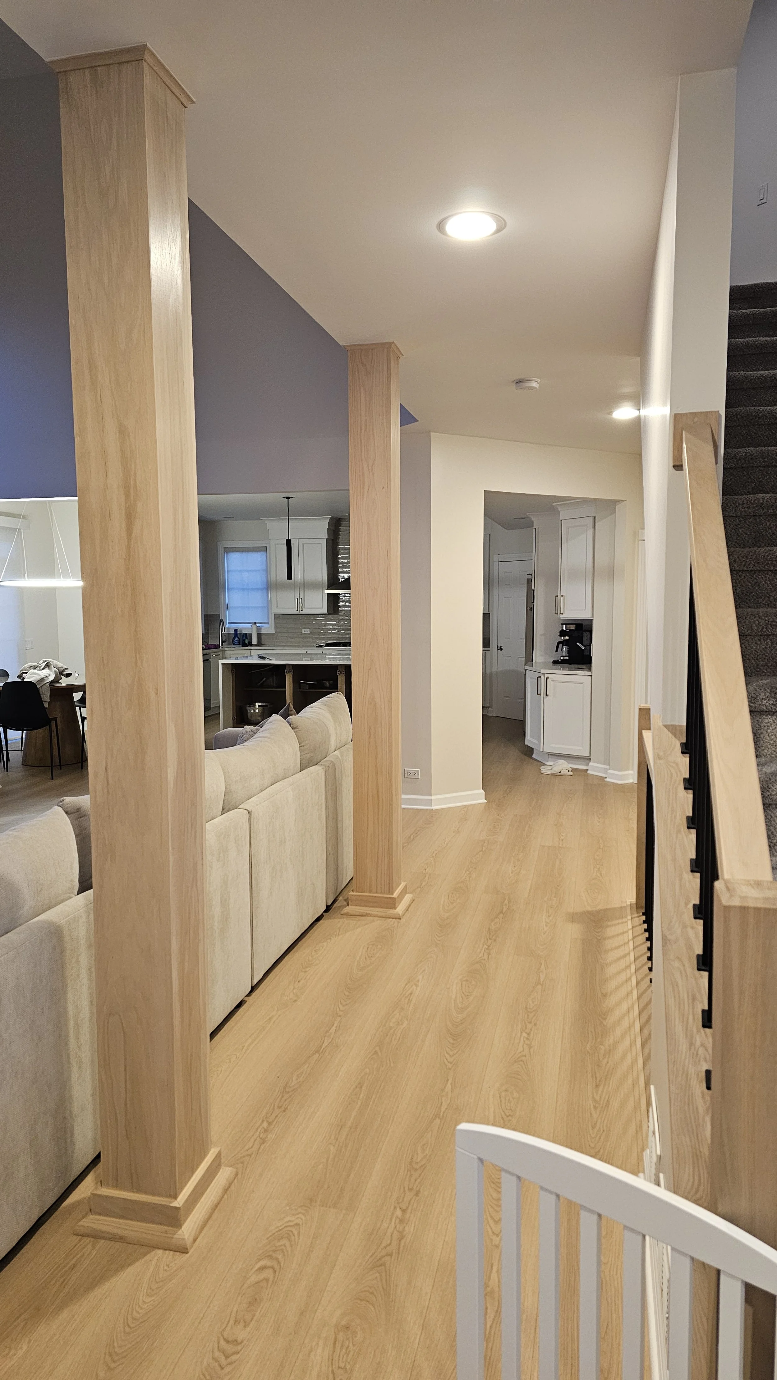 Open-concept living space with beige sofas, a kitchen with white cabinetry, and wooden floor and support beams.