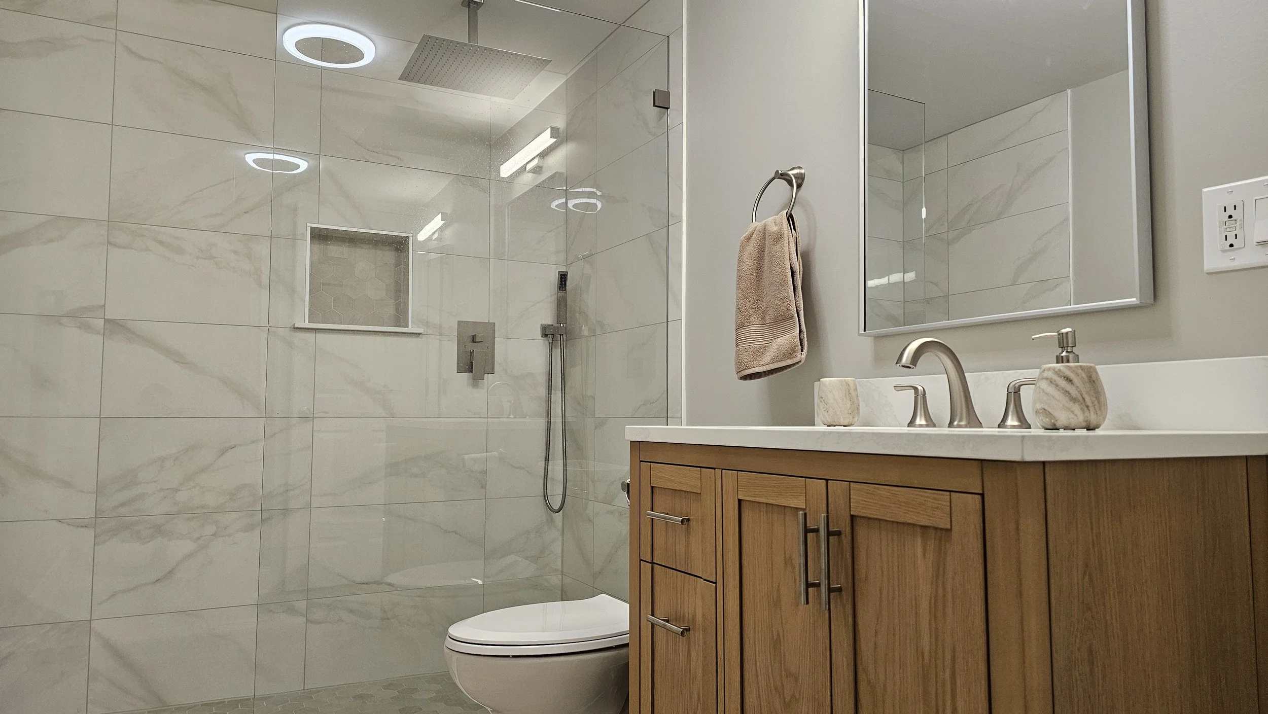Modern bathroom with a walk-in shower with glass enclosure, a toilet, and a wooden vanity with a white countertop, faucet, and mirror.
