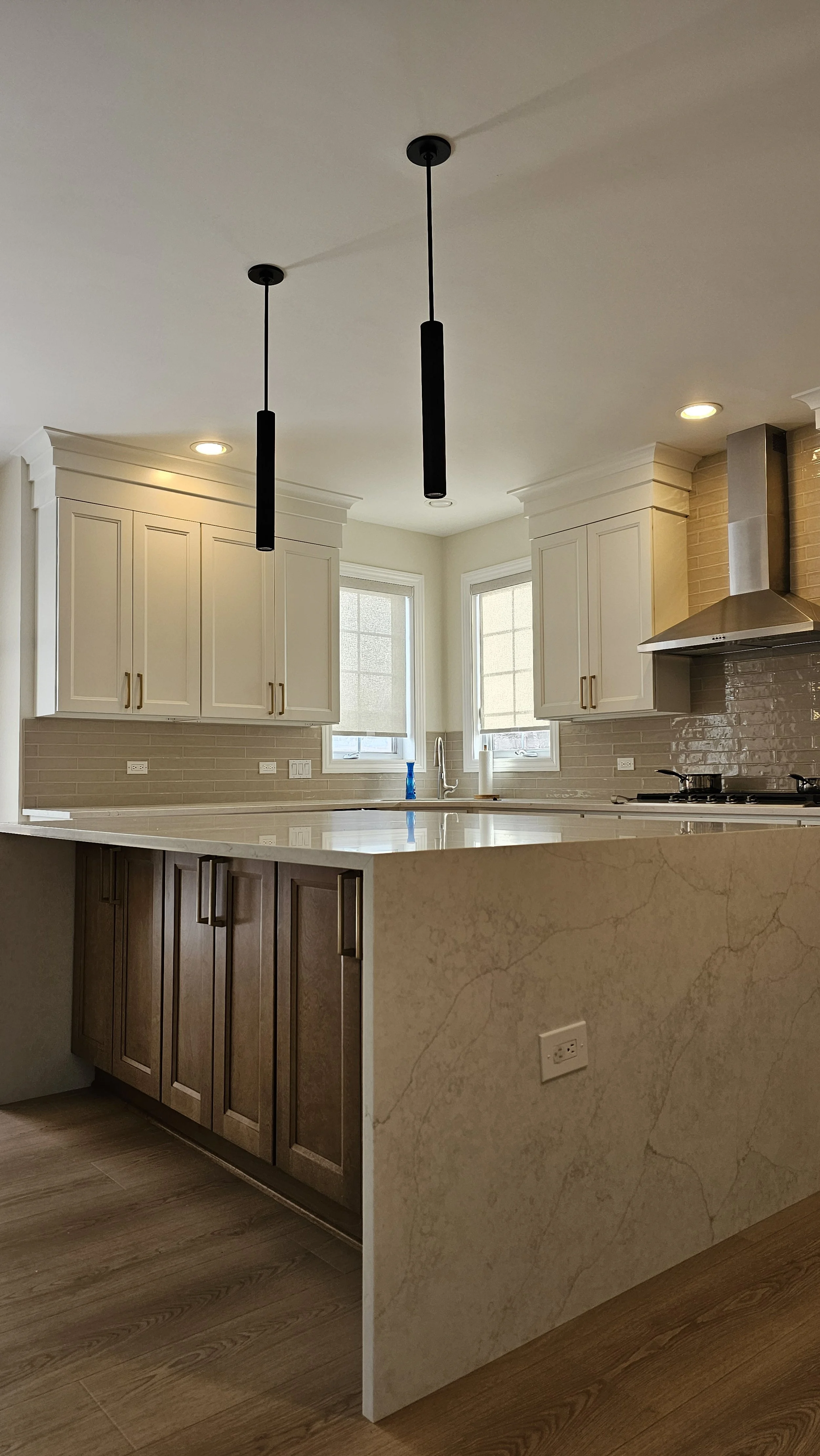 Modern kitchen with white cabinets, beige tile backsplash, a marble countertop, and pendant lights hanging from the ceiling.