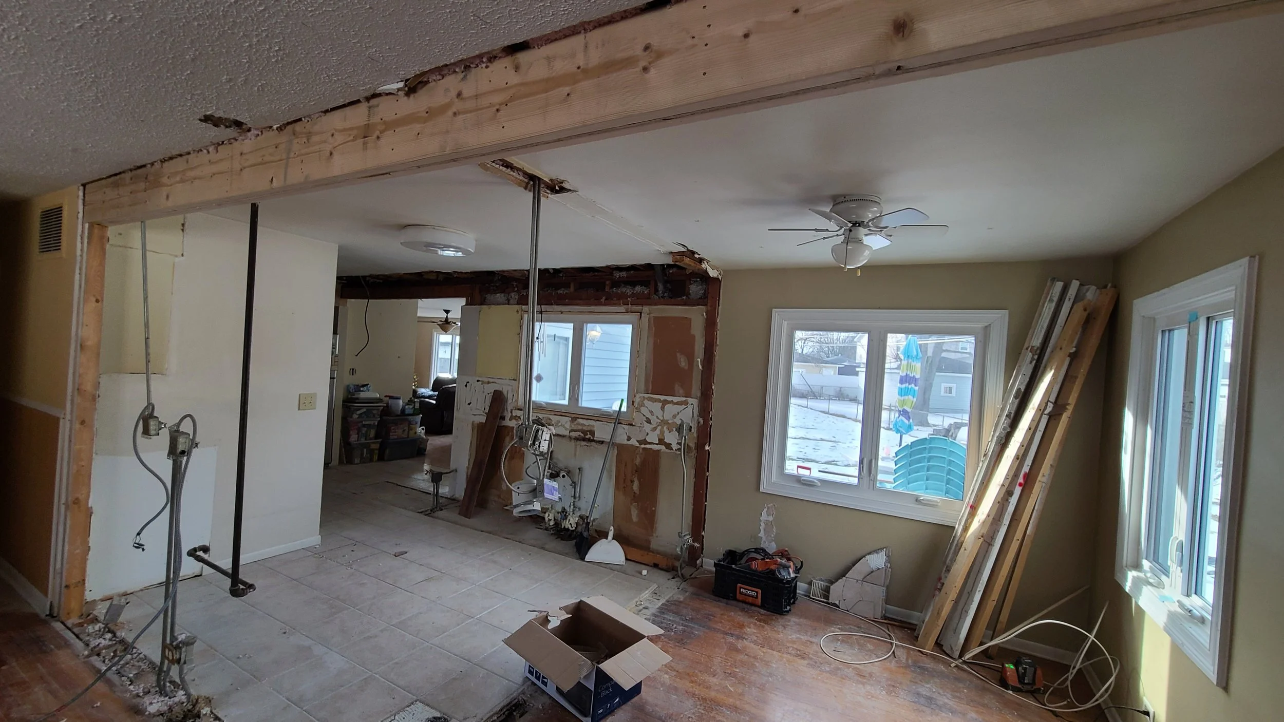 Room under renovation with missing wall, exposed framing, construction tools, and partially removed flooring.