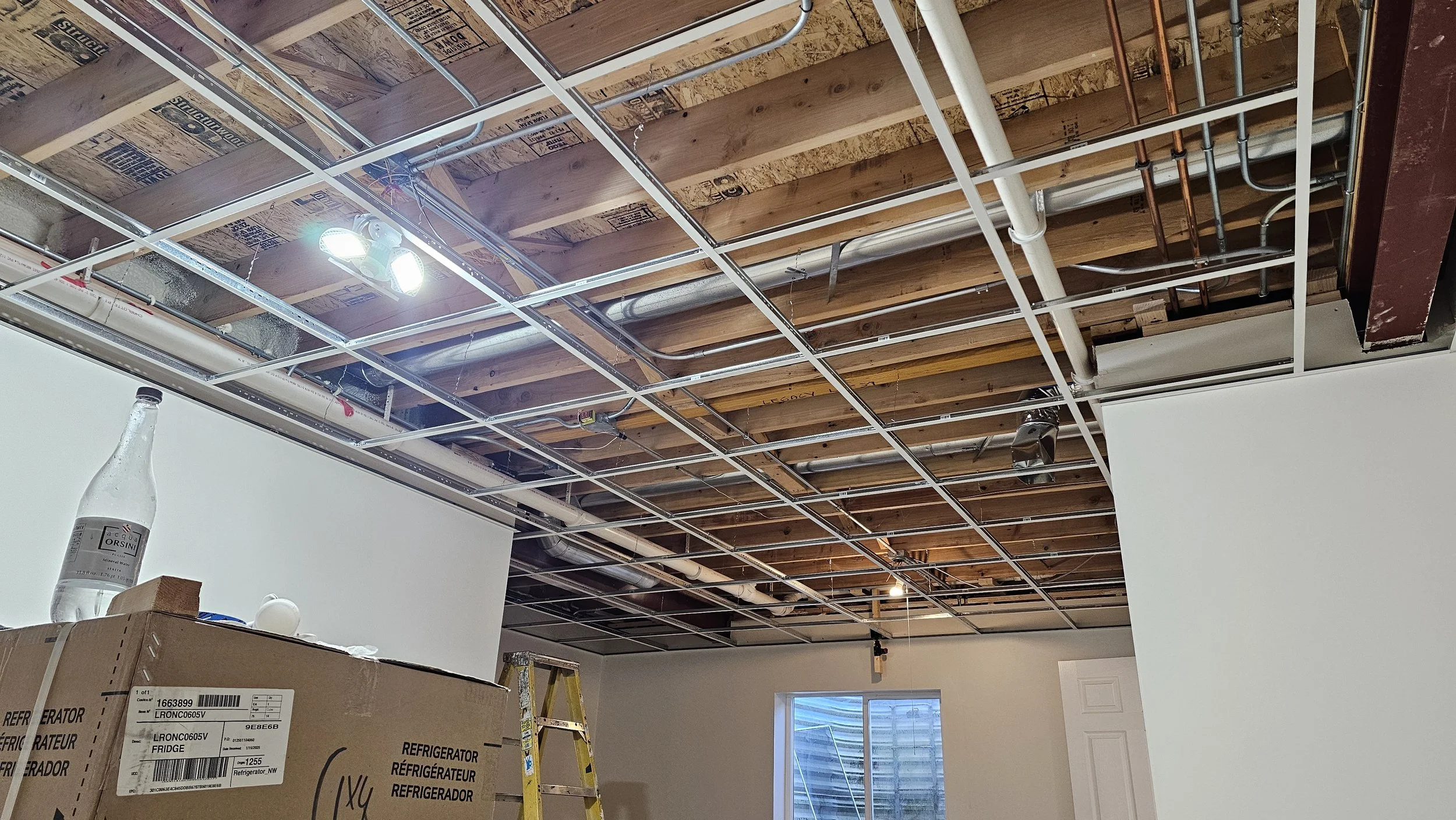 Ceiling under construction with exposed wooden beams and metal framing, tools, and construction materials in an unfinished room.