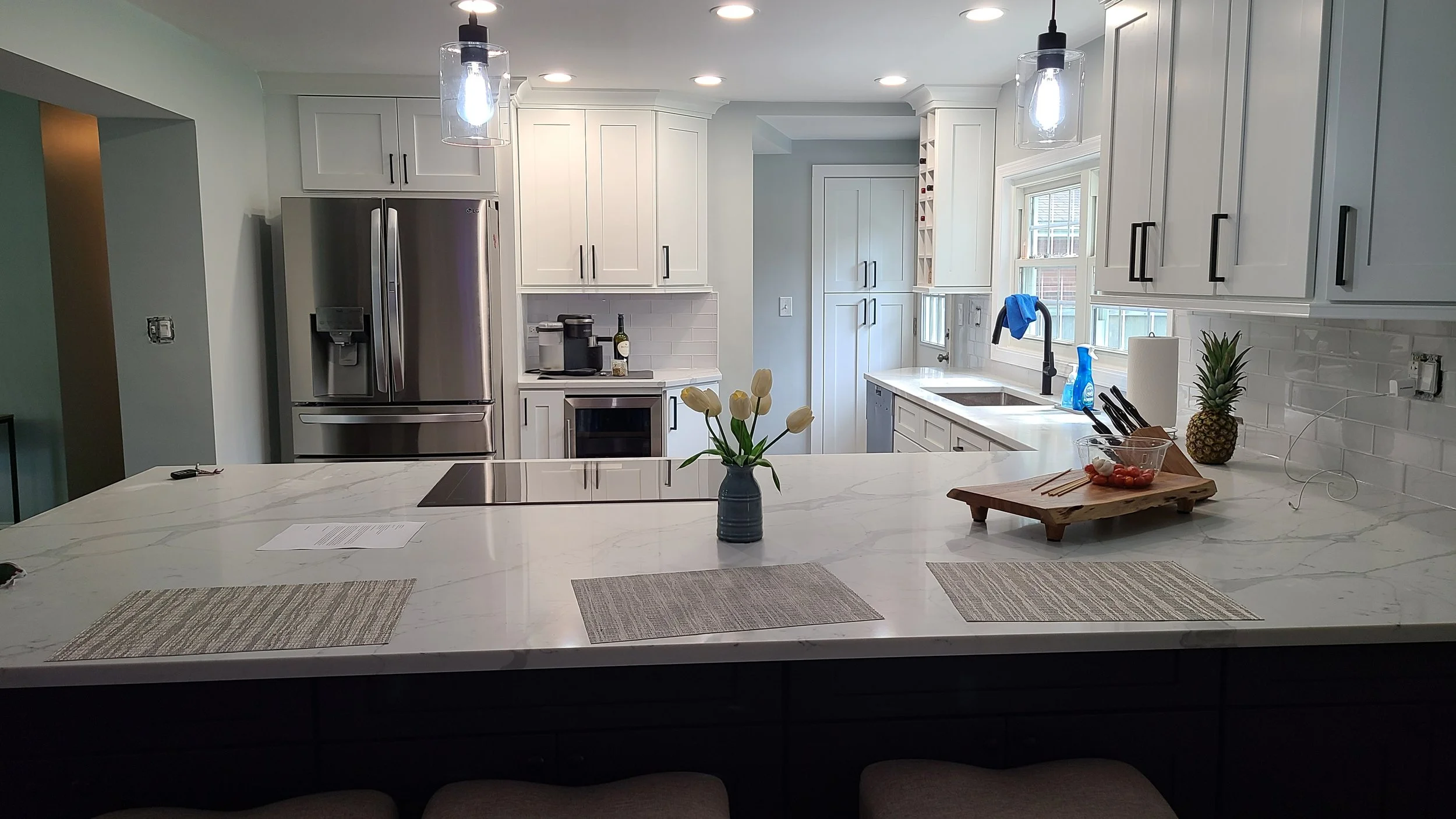 Modern kitchen with white cabinets, a large marble countertop island, a stainless steel refrigerator, and pendant lighting.