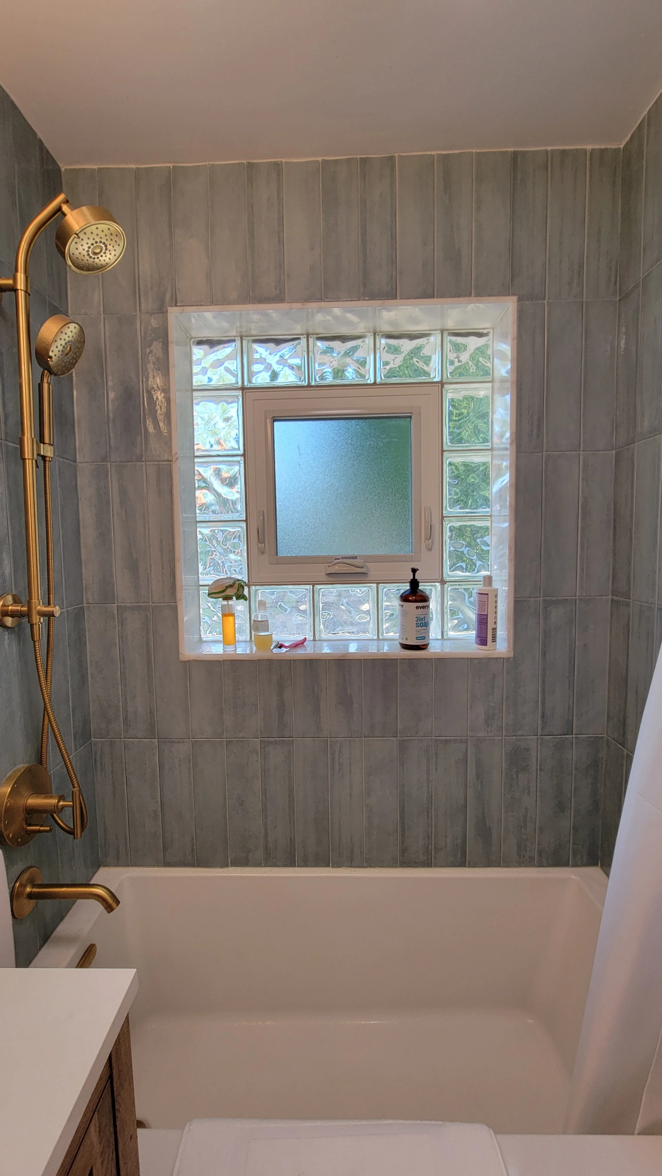Bathroom with a bathtub, a window with frosted glass and glass block framing, and a showerhead with multiple sprays in a brass finish