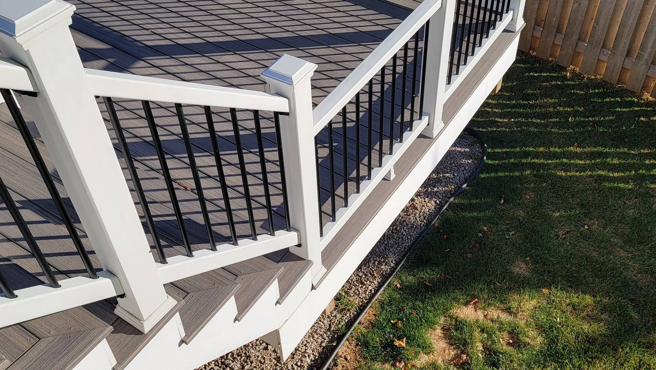 Close-up of a modern outdoor deck railing with white posts and black metal balusters, overlooking a grassy yard.