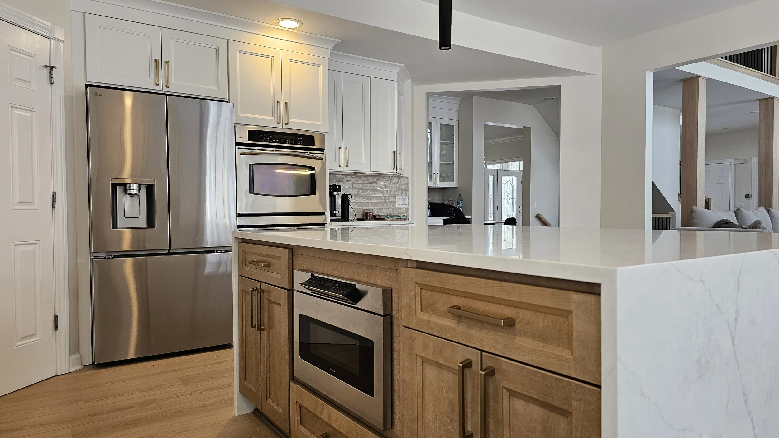 Modern kitchen with white cabinets, stainless steel refrigerator and oven, wooden lower cabinets, and a white marble countertop with an island.