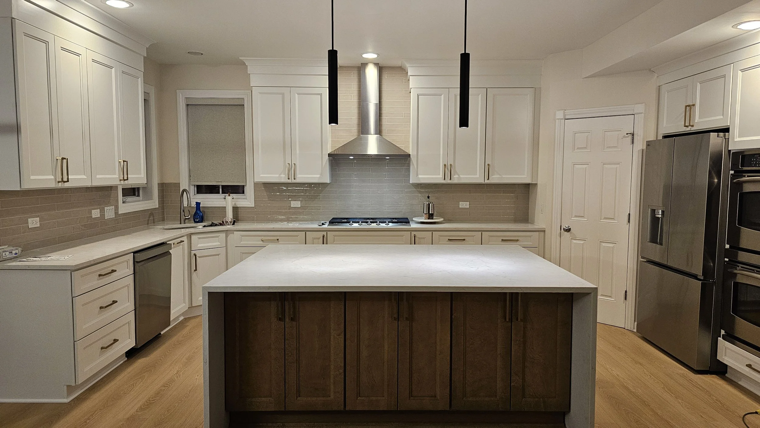 Modern kitchen with white cabinets, stainless steel appliances, a central island with a dark wood base, beige subway tile backsplash, and hardwood floors.