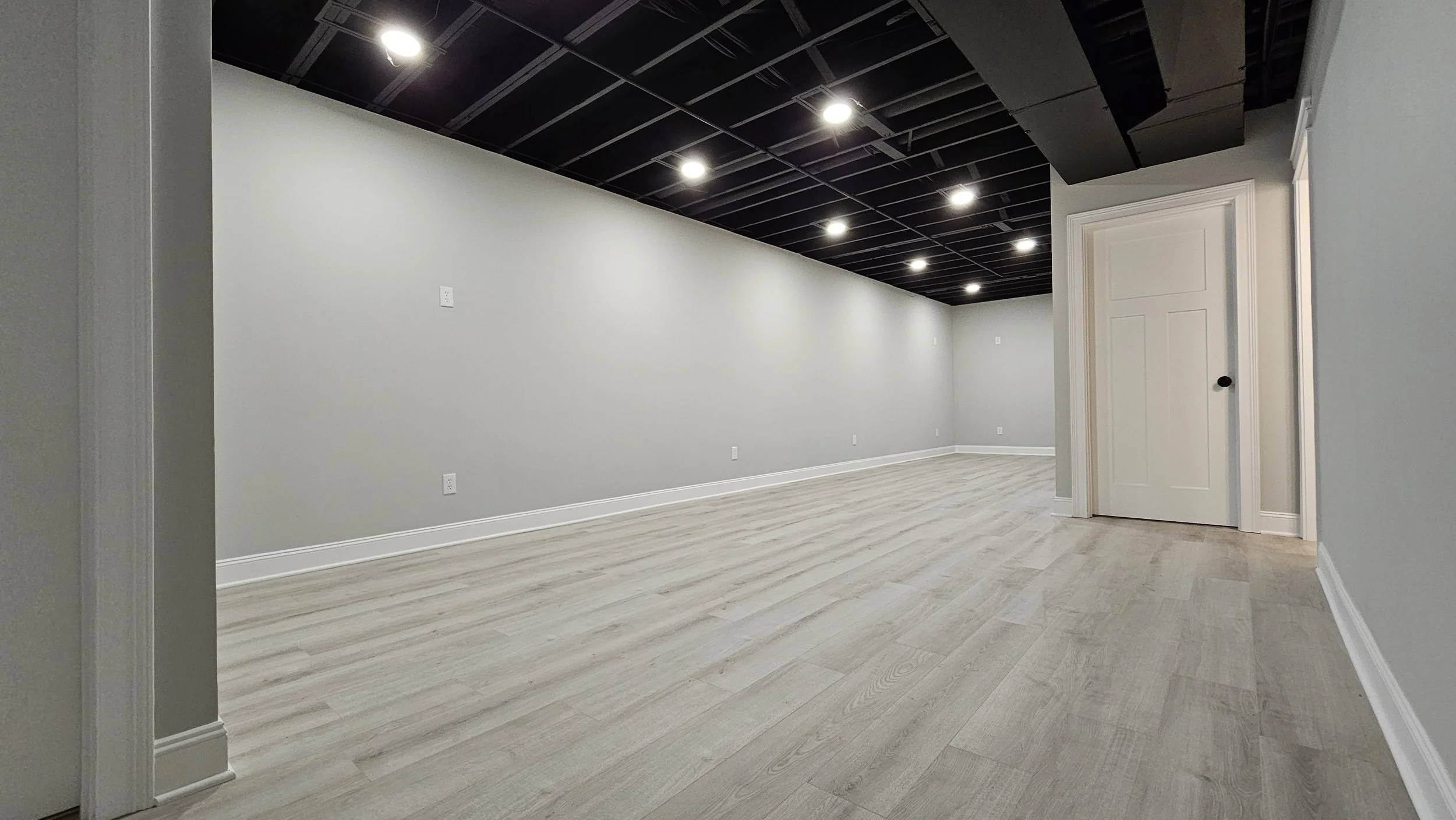 Empty room with light wood flooring, gray walls, a black ceiling with recessed lighting, and a white door.
