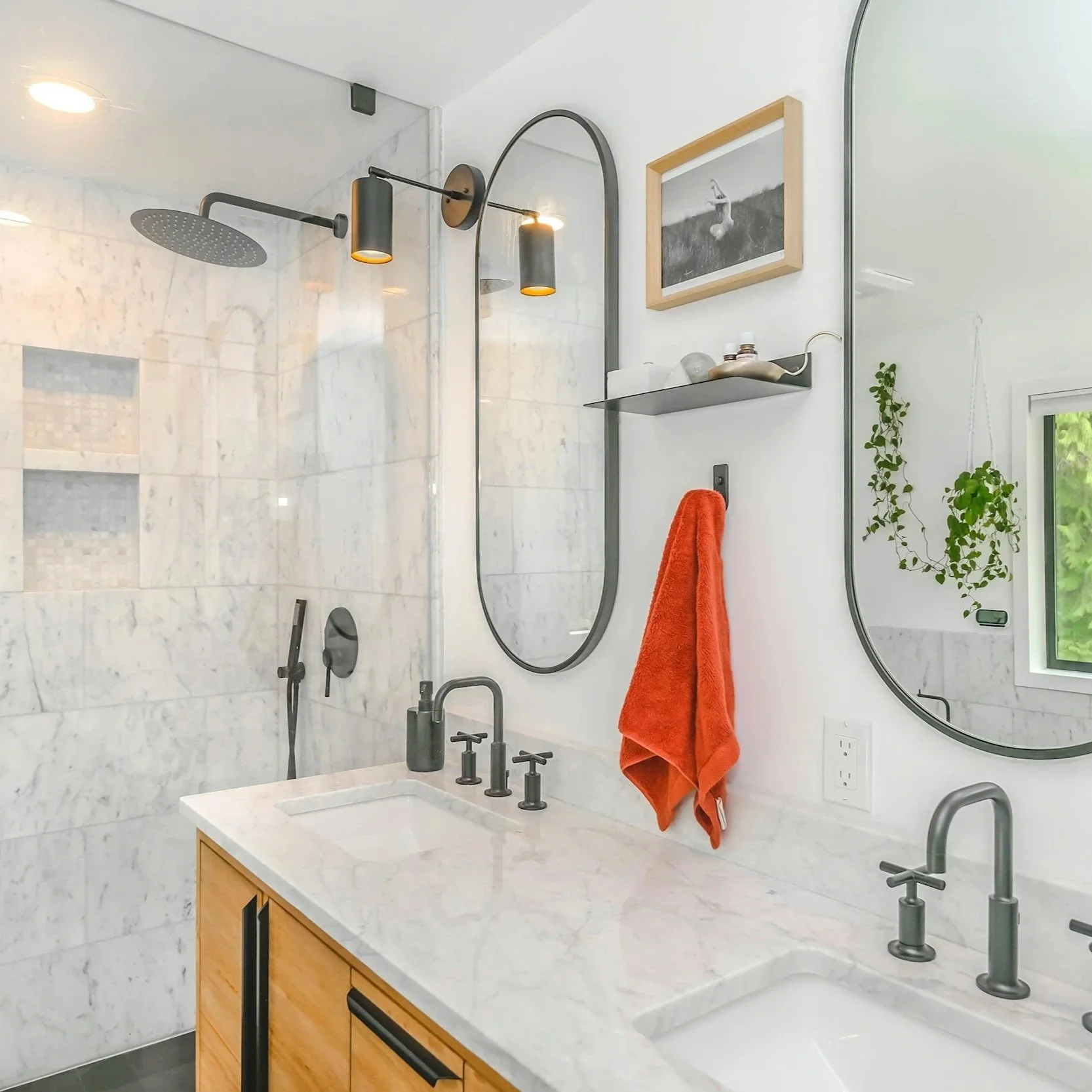 Modern bathroom with marble walls and countertops, black fixtures, two oval mirrors, a shower area, and potted plants.