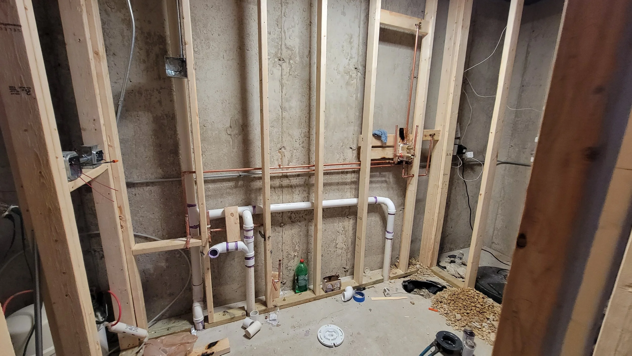 Construction site with exposed wooden studs, plumbing pipes, electrical wires, and construction tools on the floor.