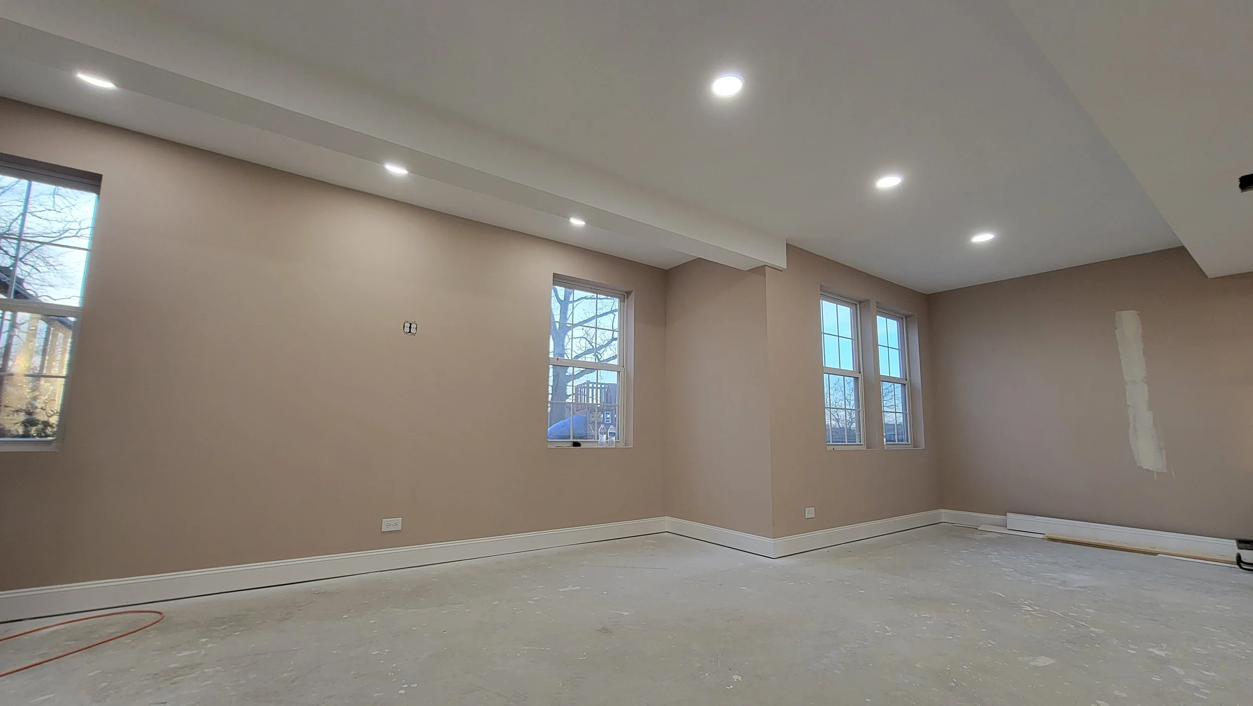 Empty room under construction with beige walls, three windows, and recessed ceiling lights.