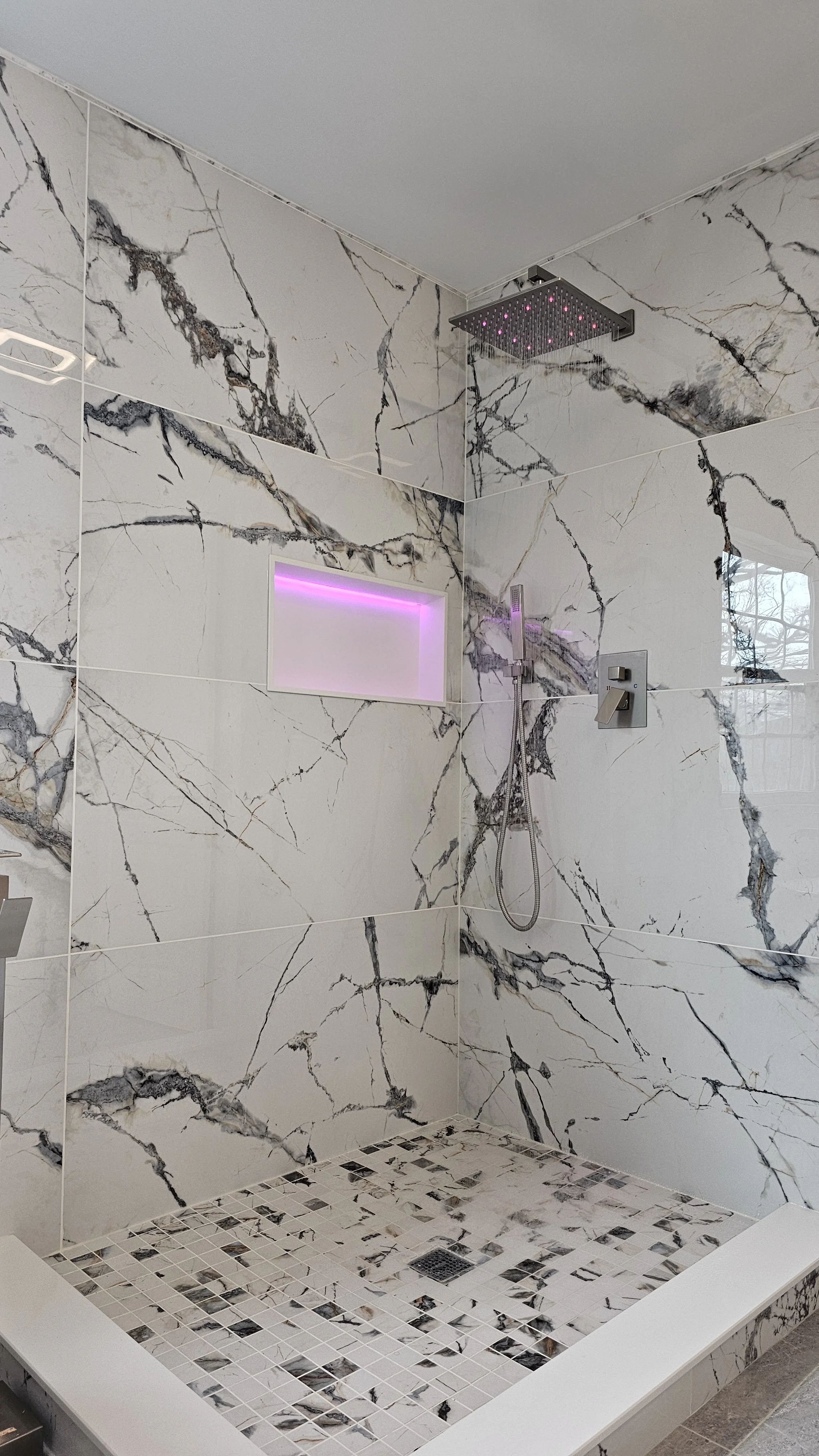 Modern marble shower with built-in niche and pink accent lighting, rainfall showerhead, and handheld shower.
