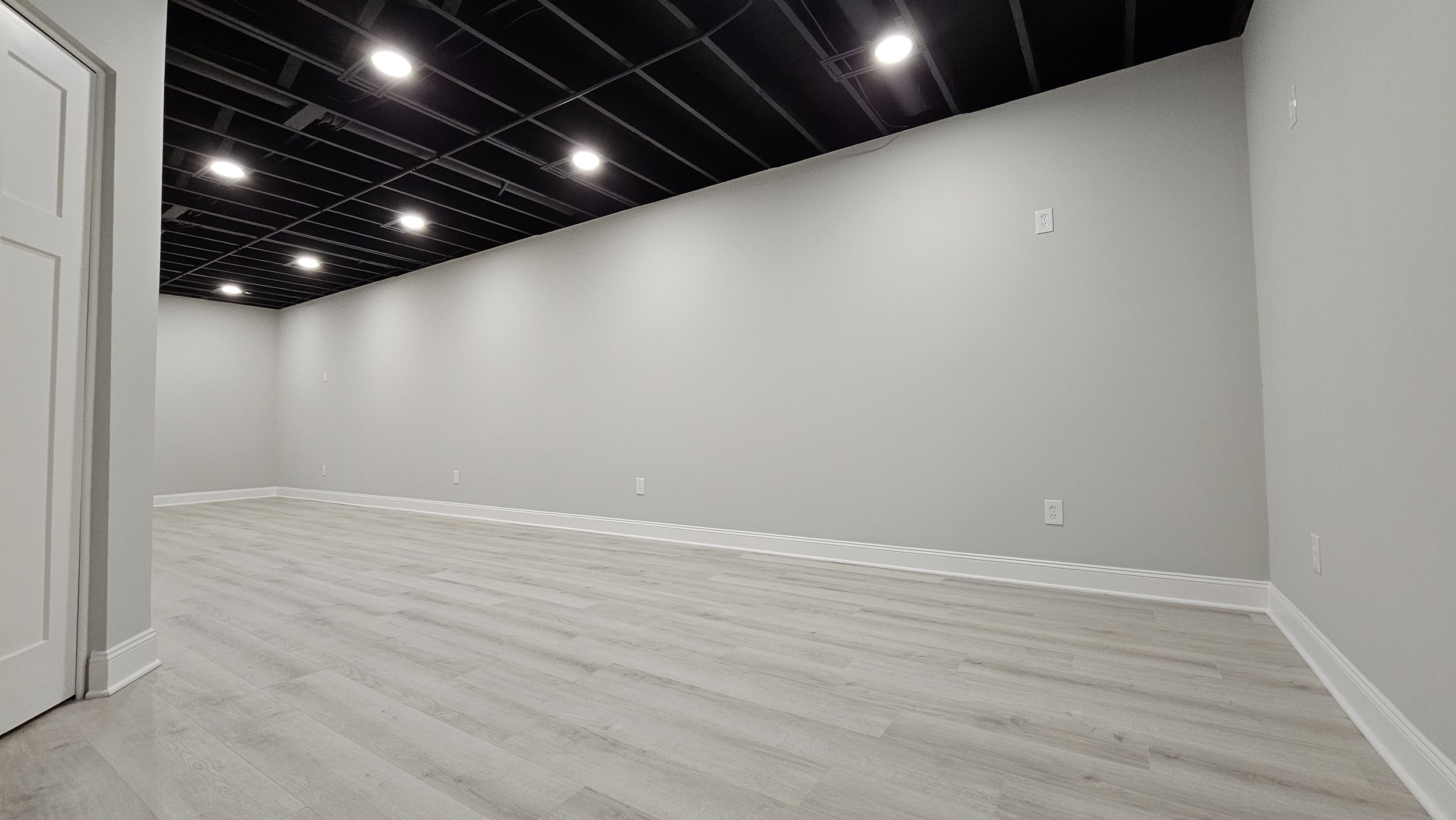 Empty room with light wood flooring, gray walls, and black ceiling with recessed lighting.