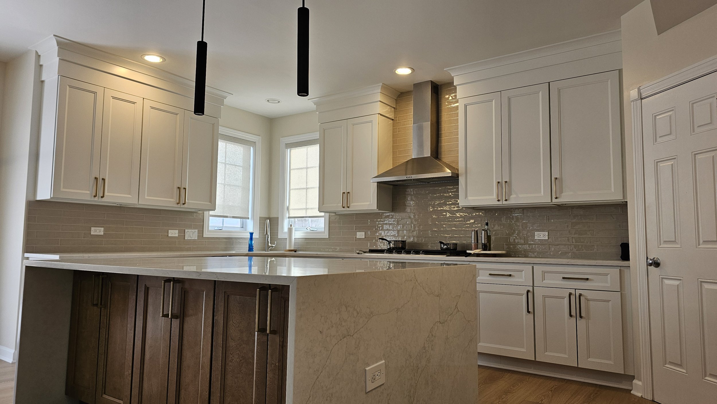 Kitchen remodel in Crystal Lake featuring white and brown cabinetry, brand new appliances, and a large island with high-end quartzite waterfall countertops.