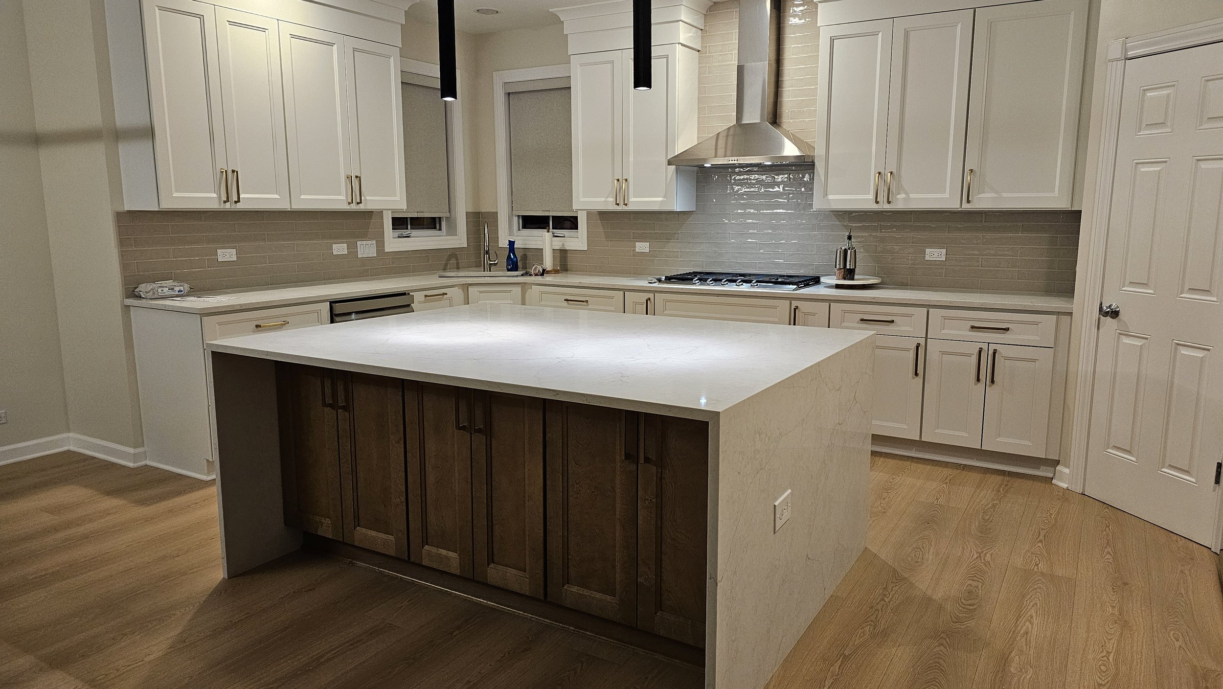 Modern kitchen with white cabinets, a large white marble island, stainless steel appliances, and light hardwood floors.