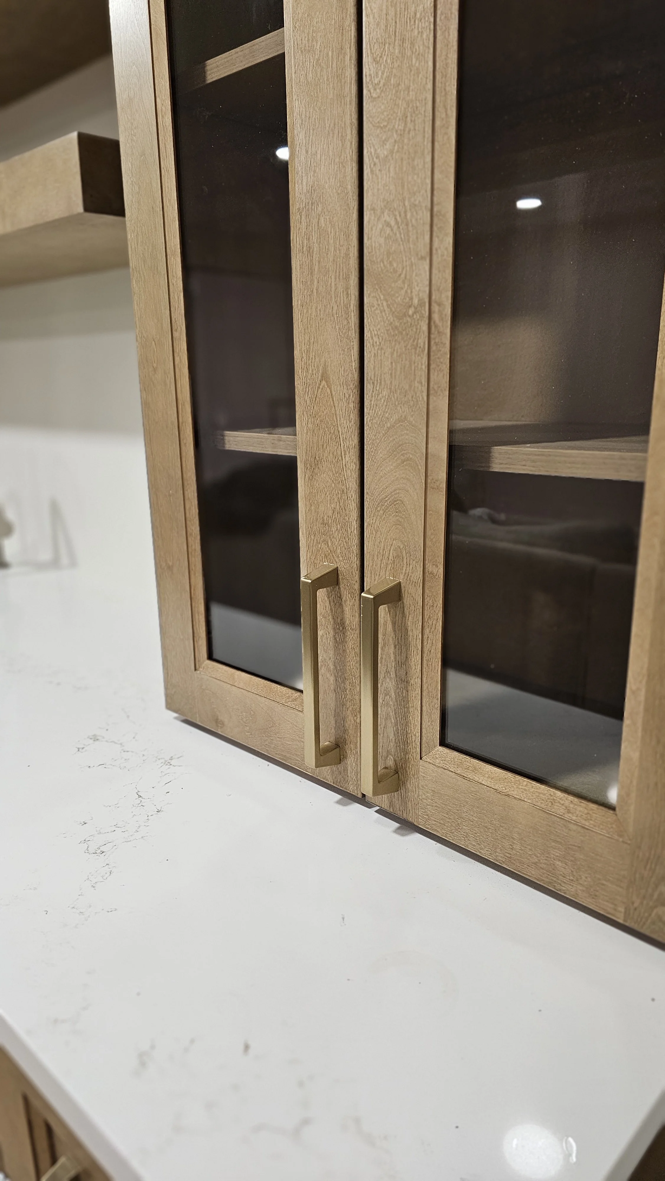Close-up of a wooden kitchen cabinet with glass doors and gold handles, mounted on a white countertop.