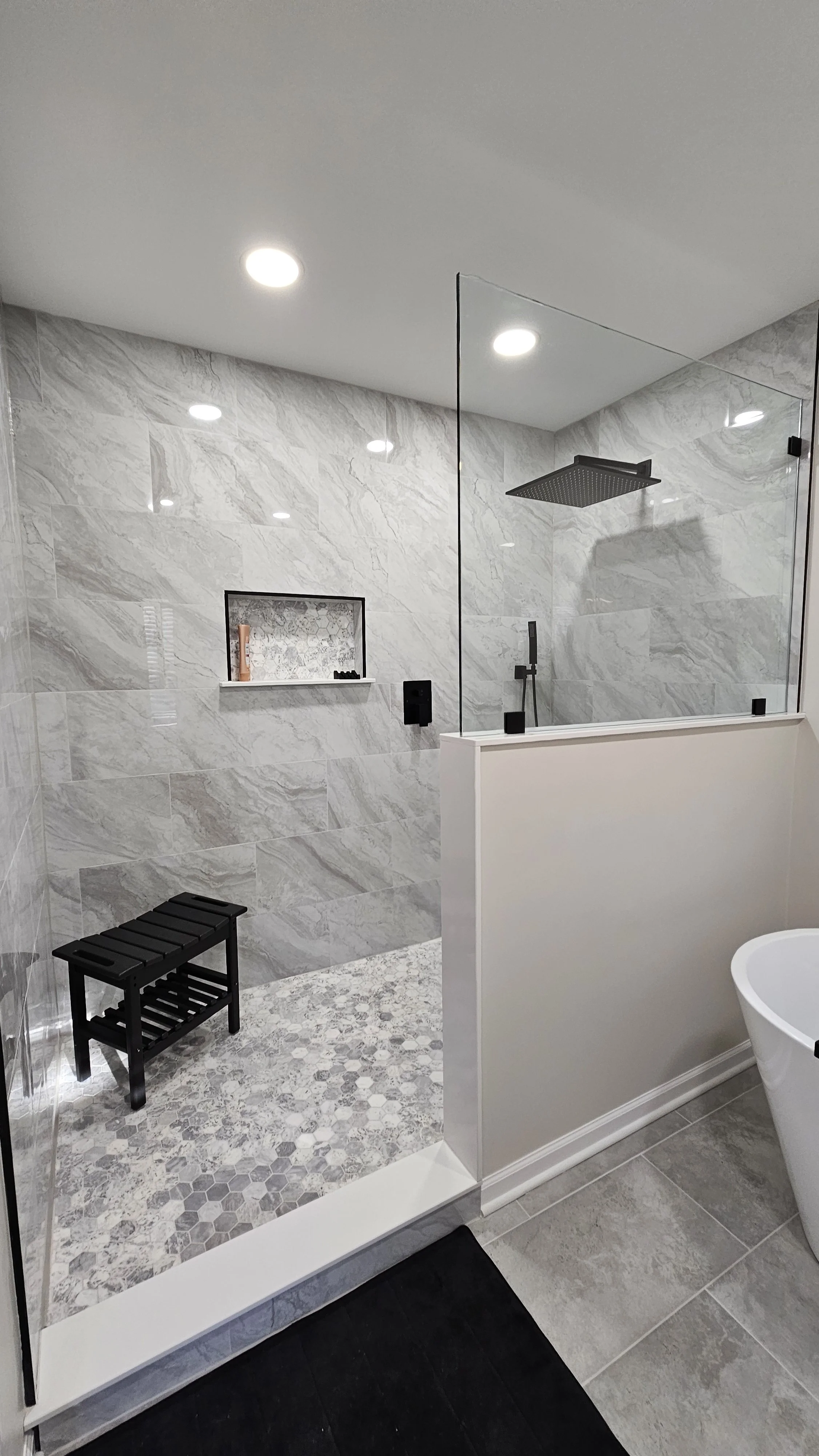 Modern bathroom with walk-in shower, black bench, marble tiles, glass shower partition, rainfall showerhead, and bathtub