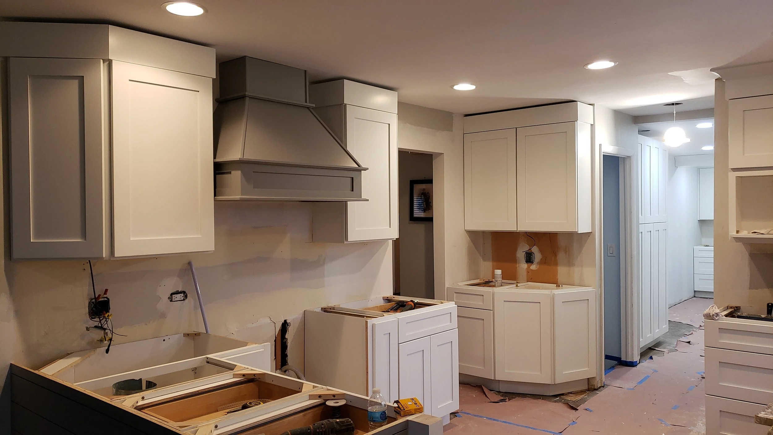 Kitchen under renovation with white cabinets and construction tools on the floor.
