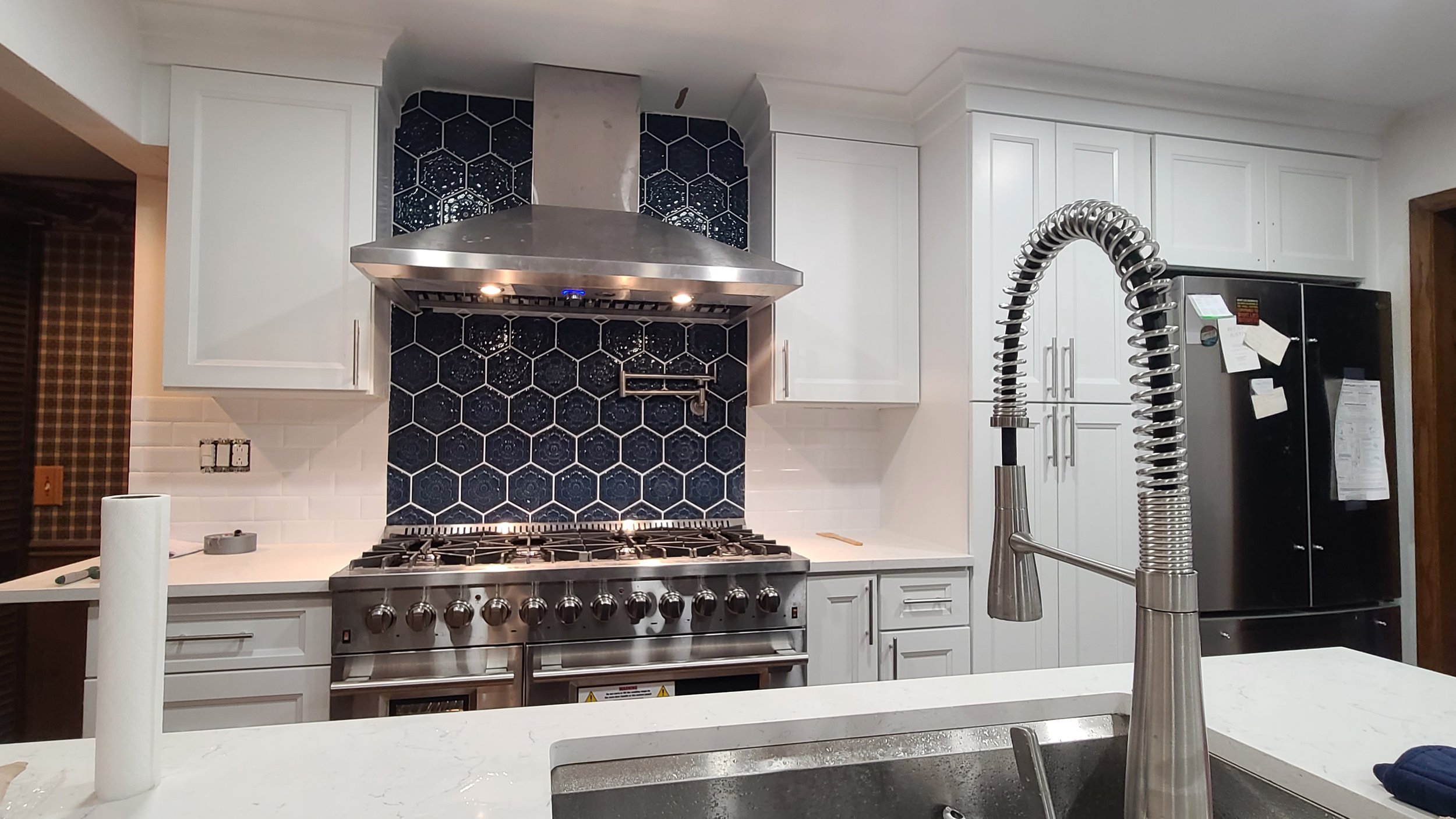 Modern kitchen with a stainless steel stove, blue hexagonal tile backsplash, white cabinets, and a black refrigerator.