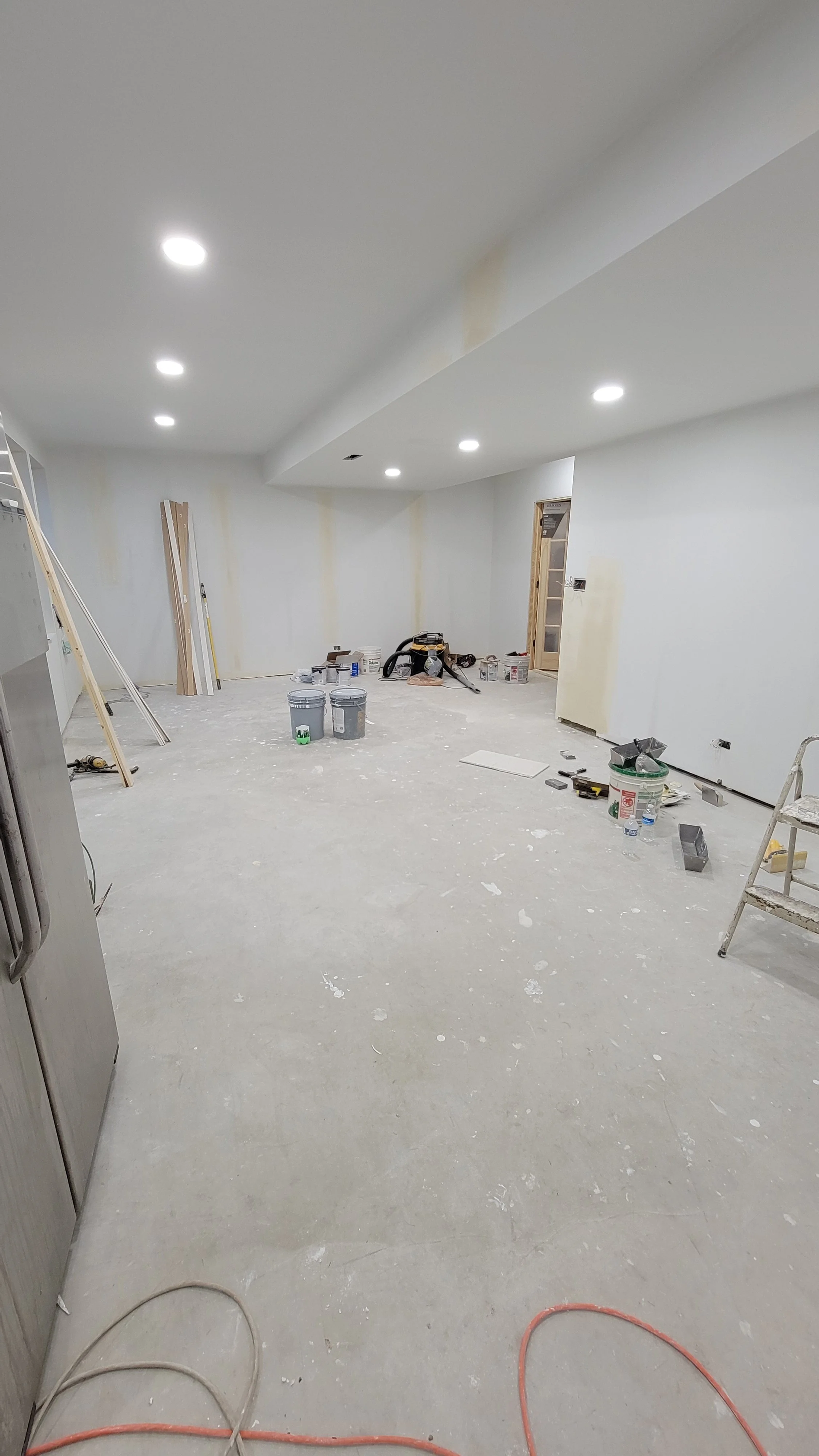 A room under construction with unfinished flooring and walls, construction tools, paint buckets, and building materials scattered around.