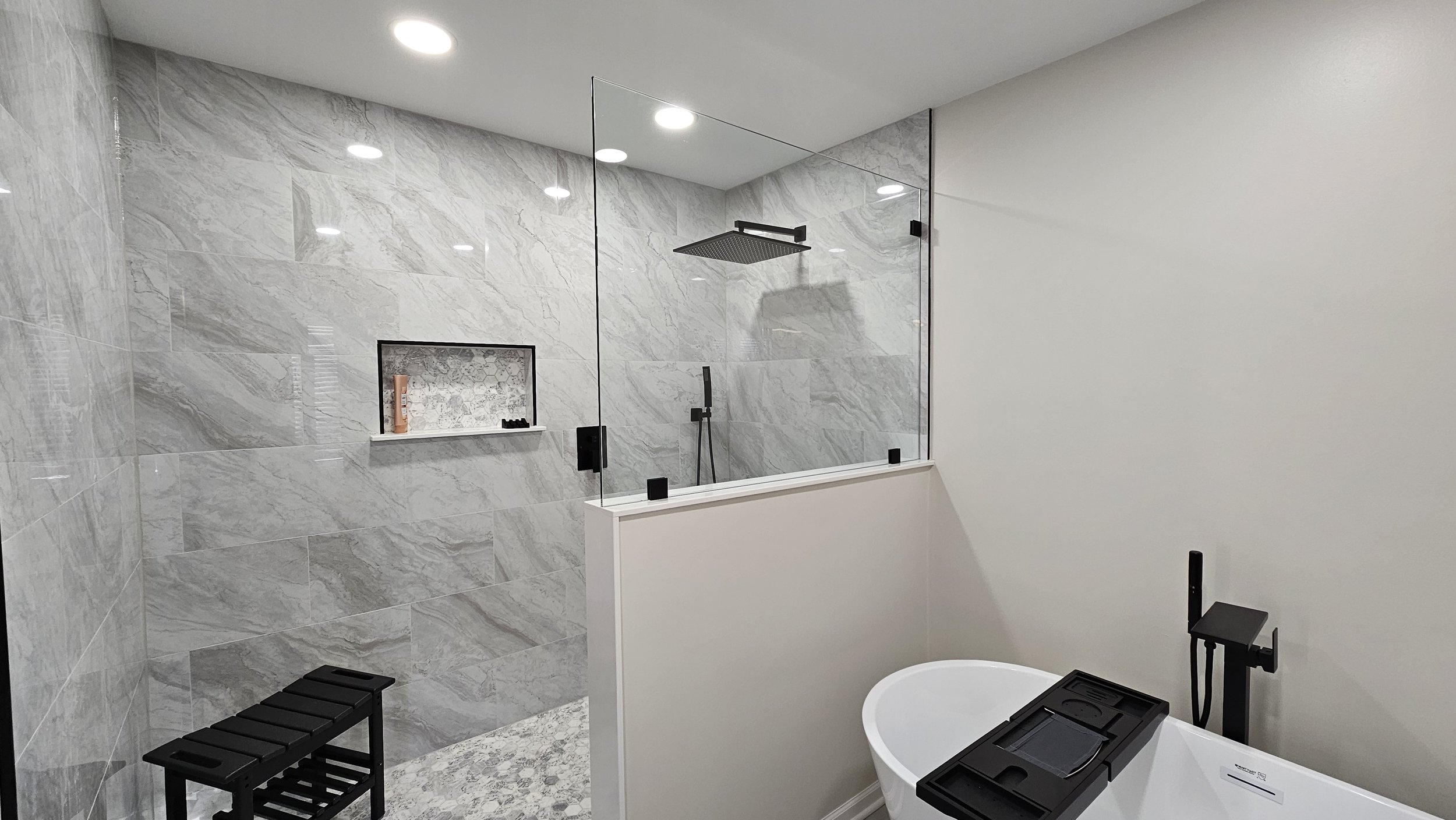 Modern bathroom with a walk-in shower enclosed by glass, a built-in shower niche, and a bathtub with a black faucet and handheld shower head.