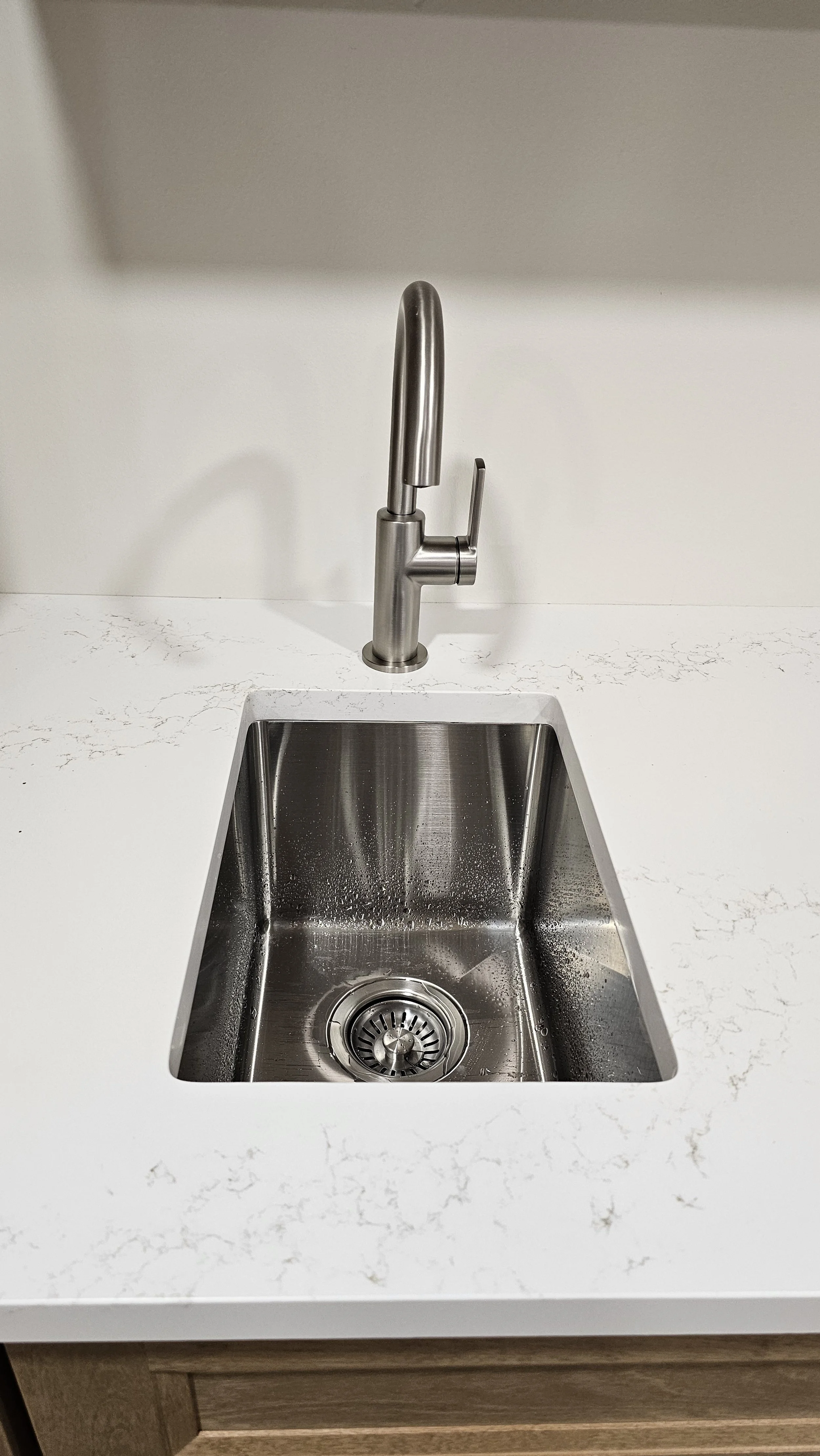 A stainless steel kitchen sink with a modern faucet on a white marble countertop.