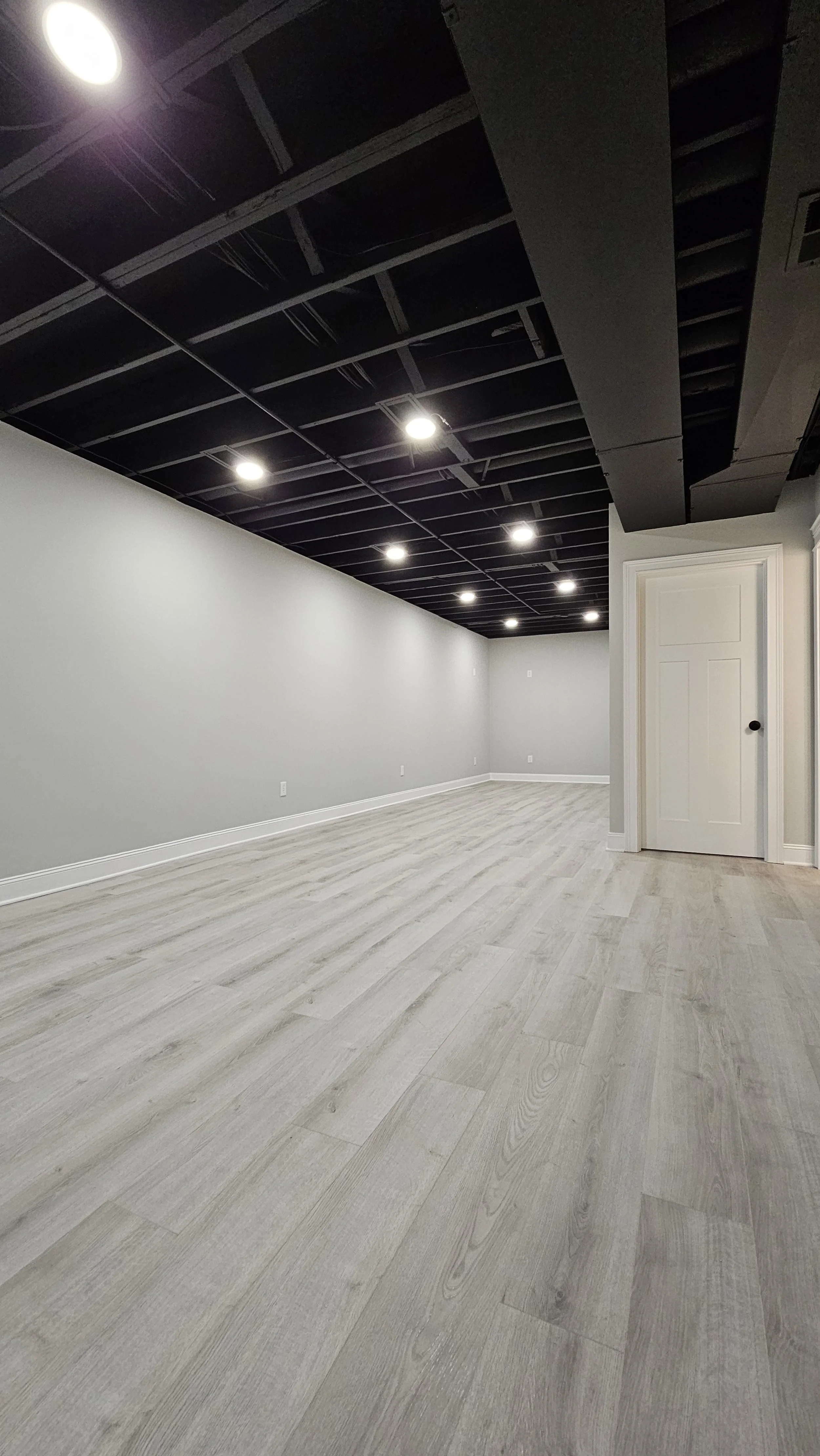 Empty room with laminate wood floors, gray walls, and a ceiling with exposed black framework and recessed lighting.