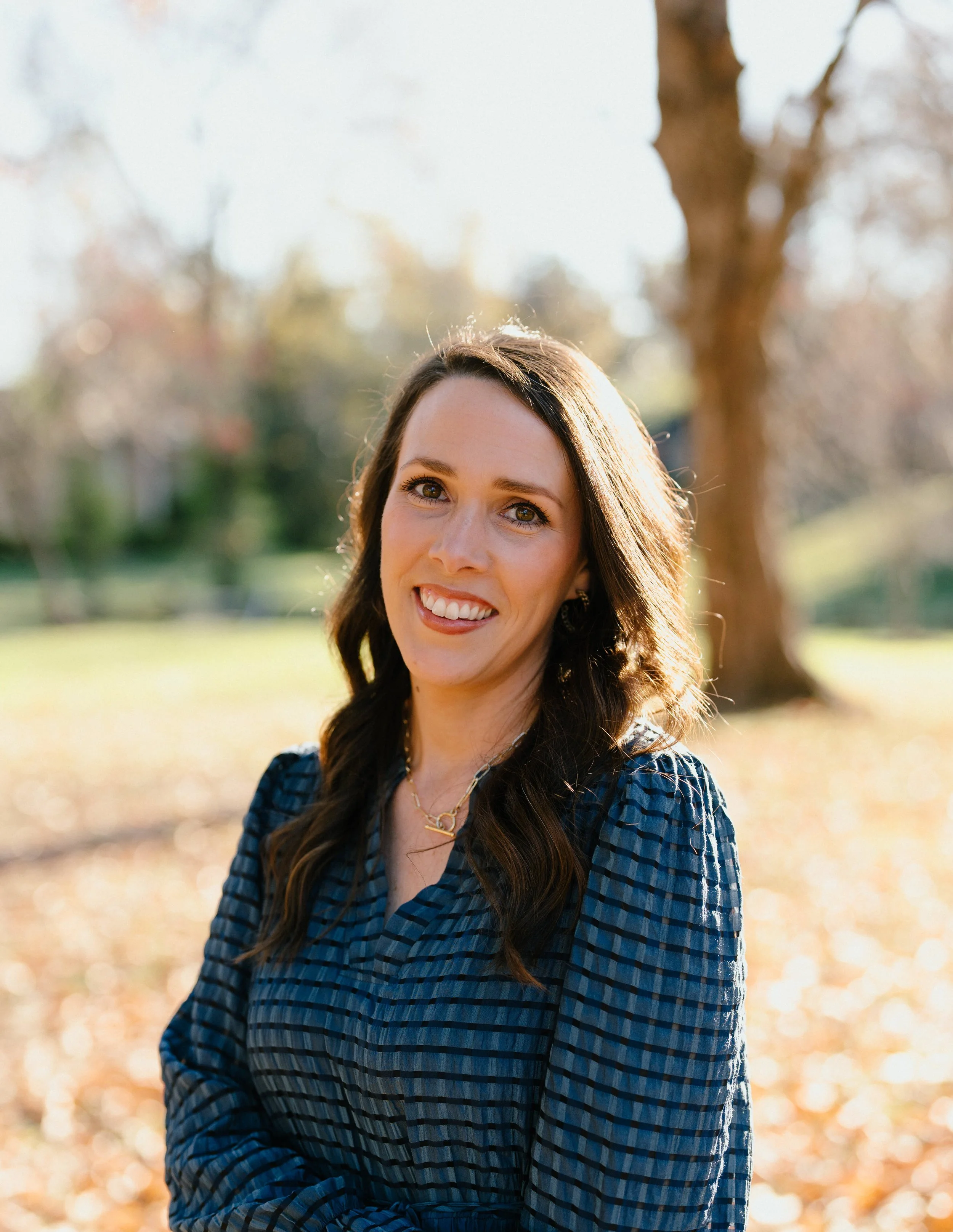 A smiling woman with dark brown hair wearing a black top and turquoise earrings.
