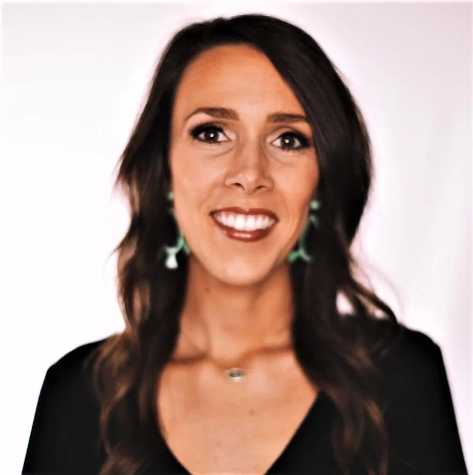 A smiling woman with dark brown hair wearing a black top and turquoise earrings.