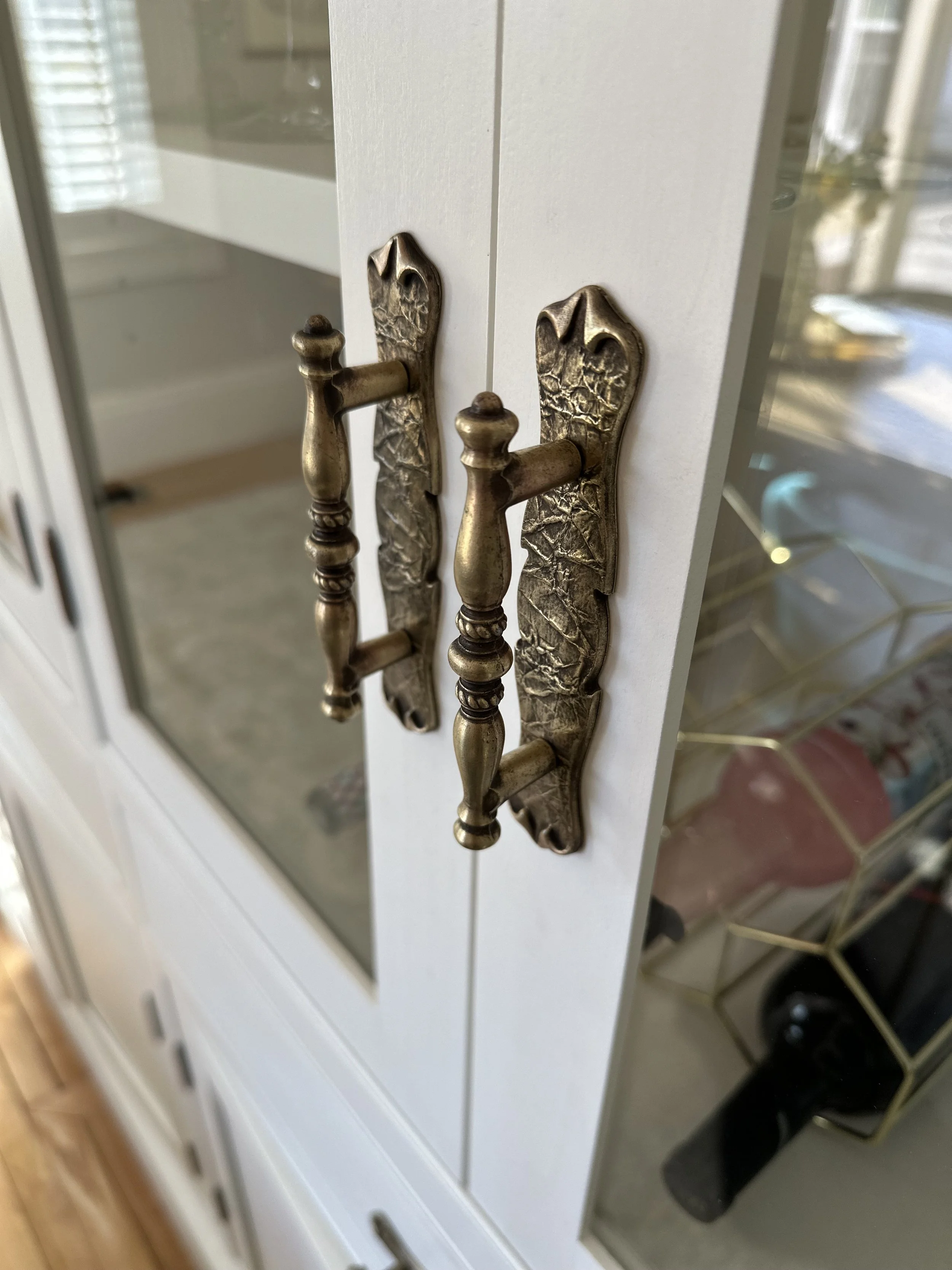 Close-up of a pair of vintage brass cabinet handles with ornate detailing on white cabinet doors.