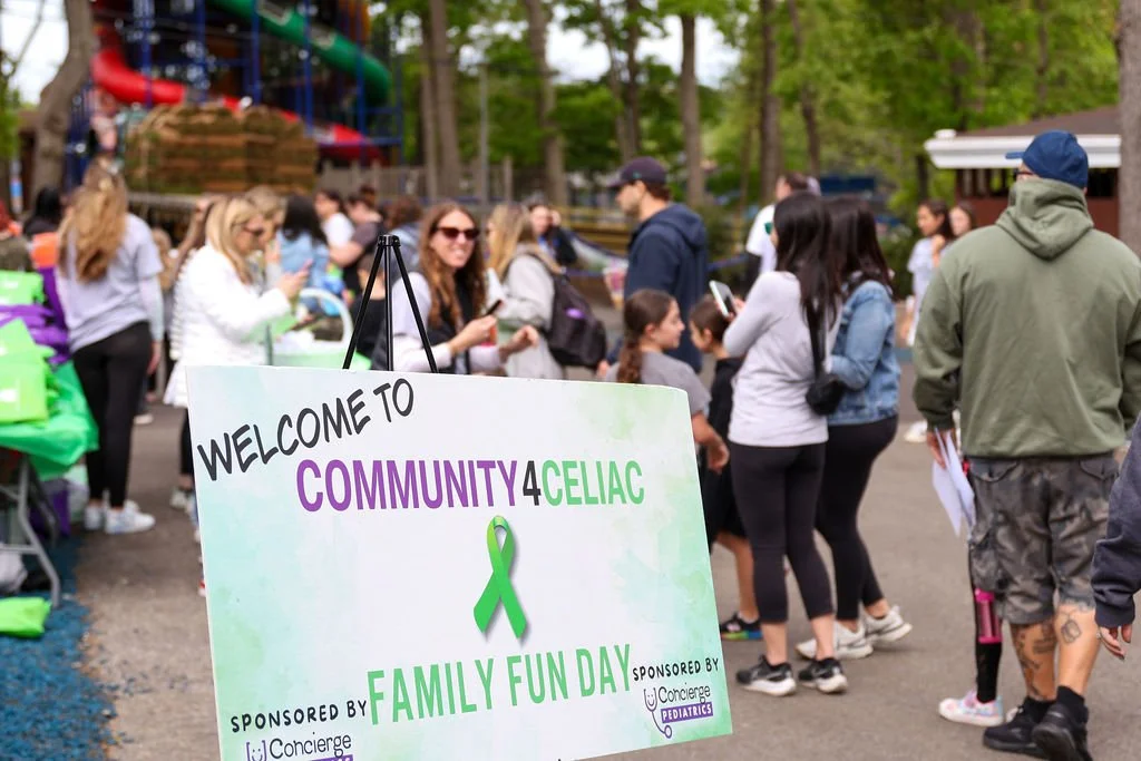 People gathered outdoors at a community event for family fun day, with a sign welcoming attendees to the event and recognizing sponsorship by Concierge Pediatrics and others.