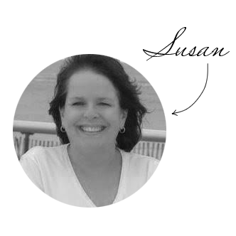 A black-and-white photo of a woman smiling outdoors, with a railing and clear sky in the background.