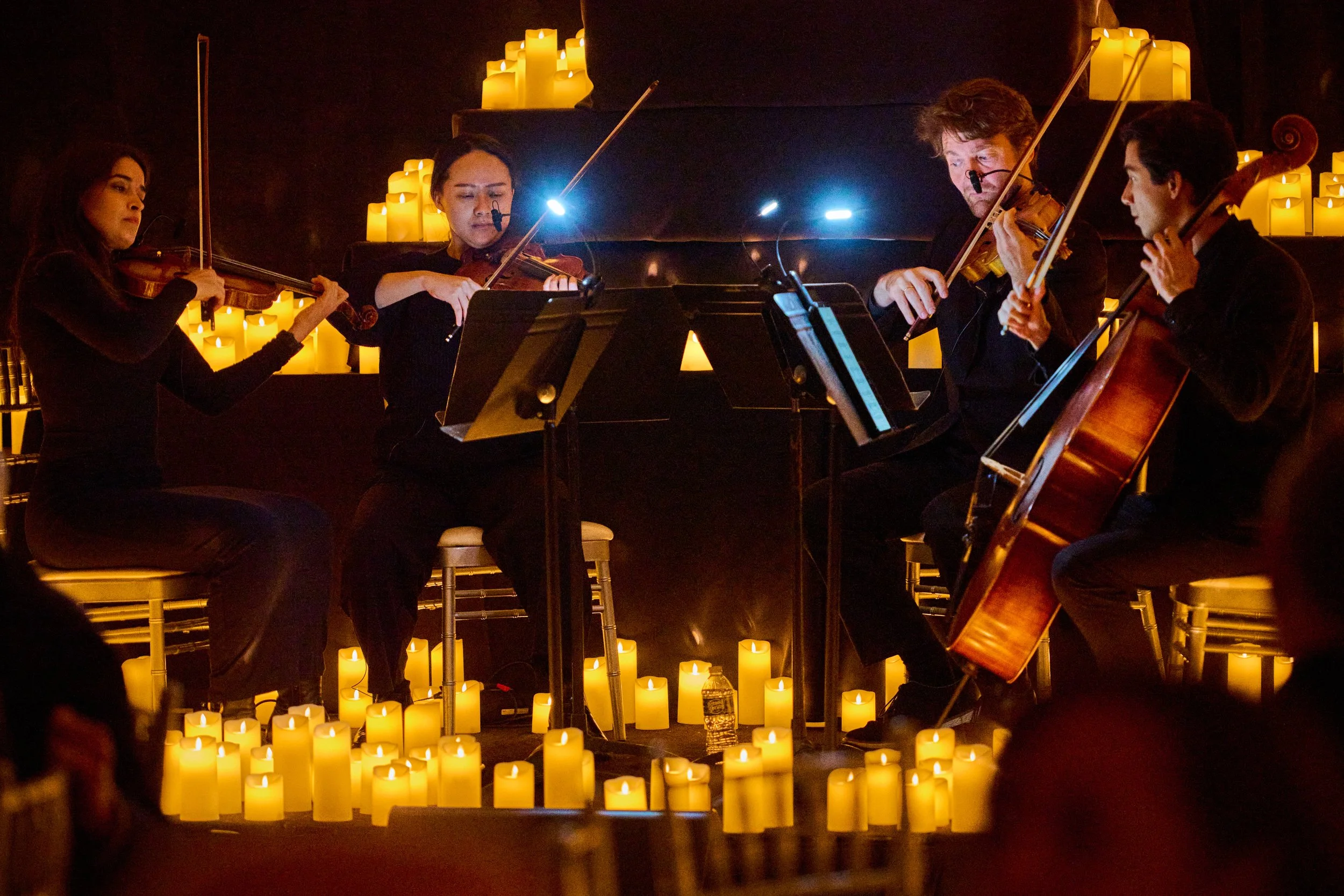 A string ensemble of four musicians performing with candles arranged around them, illuminated softly in a dark room.