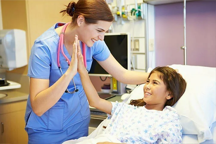 A smiling nurse giving a high five to a young girl lying in a hospital bed.
