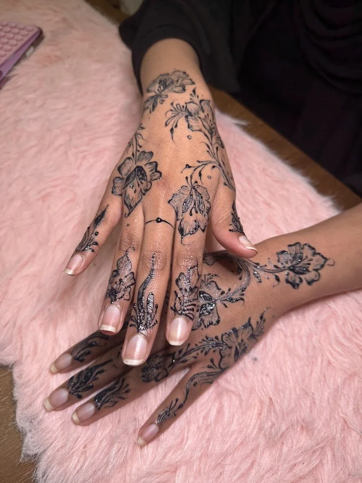 A person's hands with black floral henna tattoos resting on a pink furry surface.
