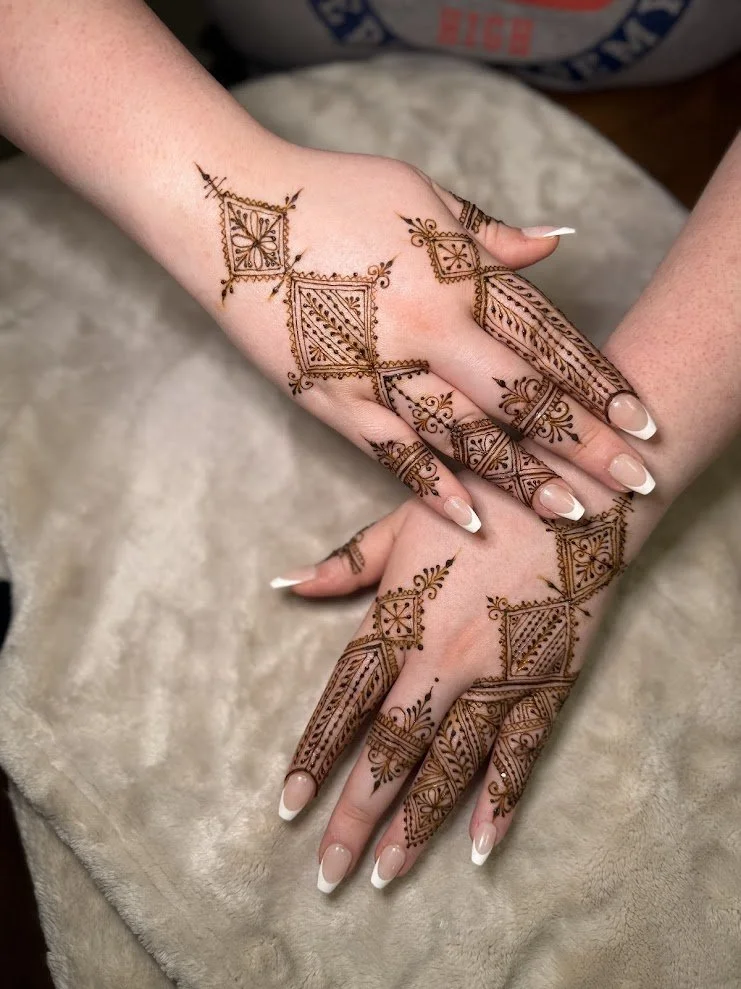 Hands decorated with intricate henna designs including squares, floral motifs, and geometric patterns.