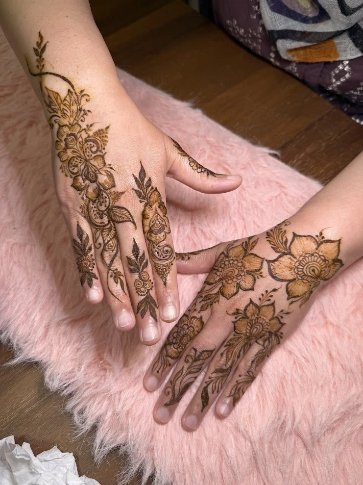Two hands with intricate henna tattoos featuring flowers and leaves, resting on a pink furry surface.