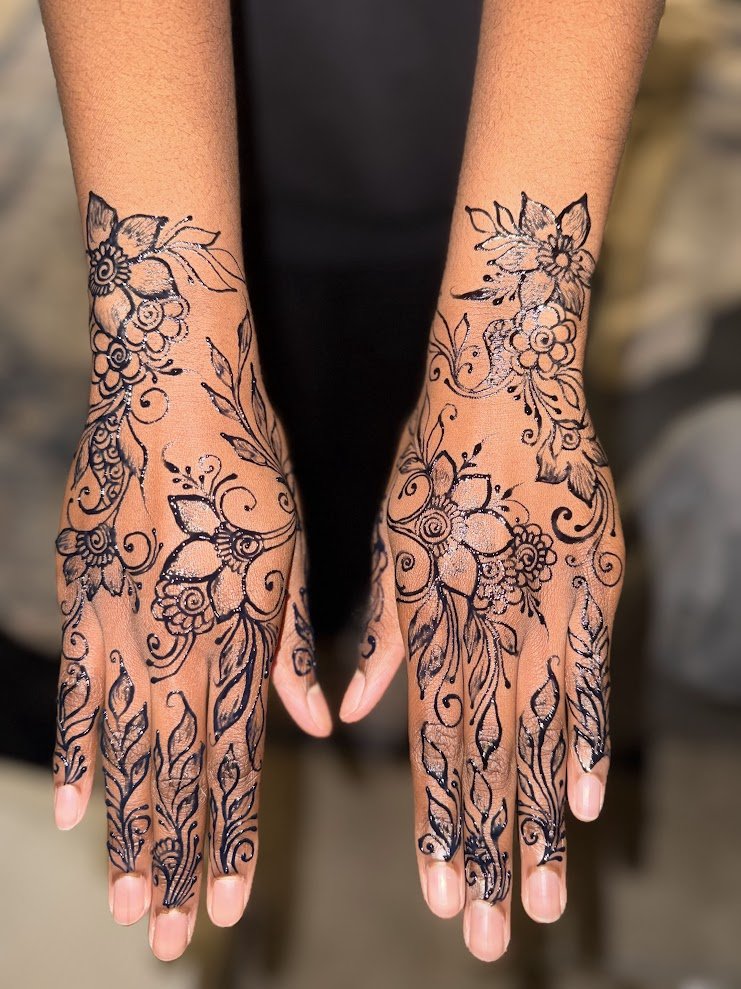 Decorative black henna tattoo designs on both hands with floral and leaf patterns.