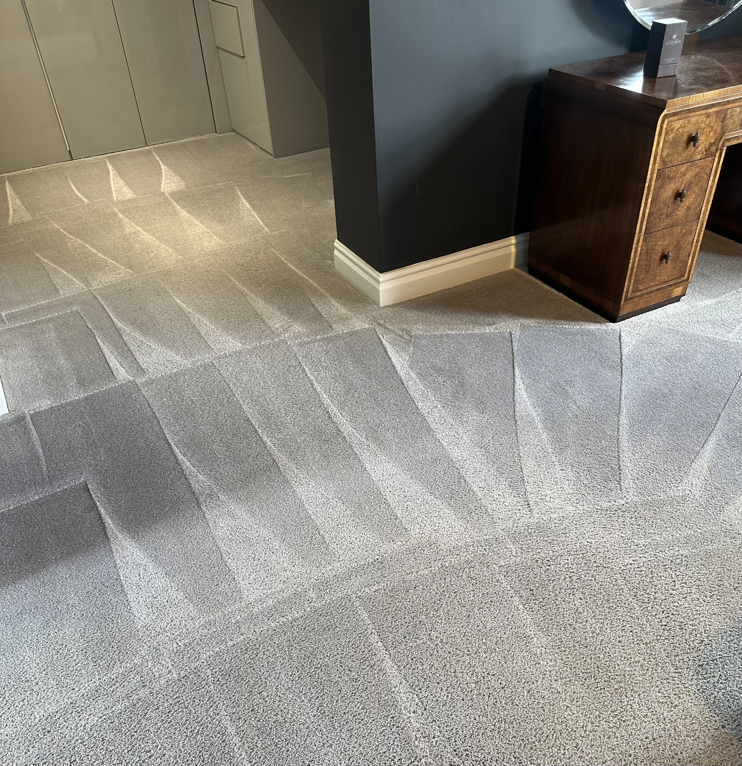 A beige carpet with visible vacuum lines in a room with a doorway, a black wall, and a wooden desk.