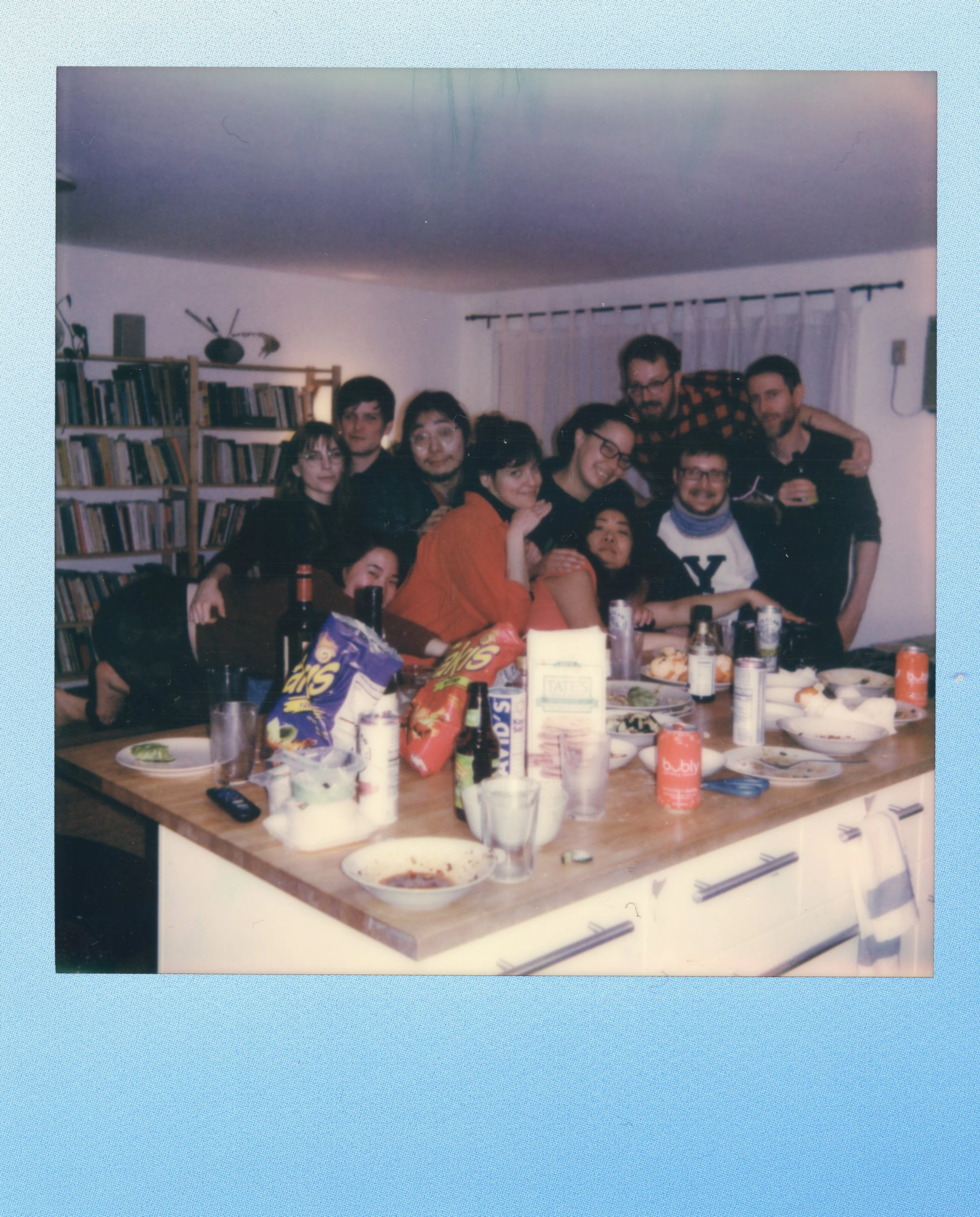 Group of people gathered in a kitchen celebrating around a table filled with snacks, drinks, and dishes.