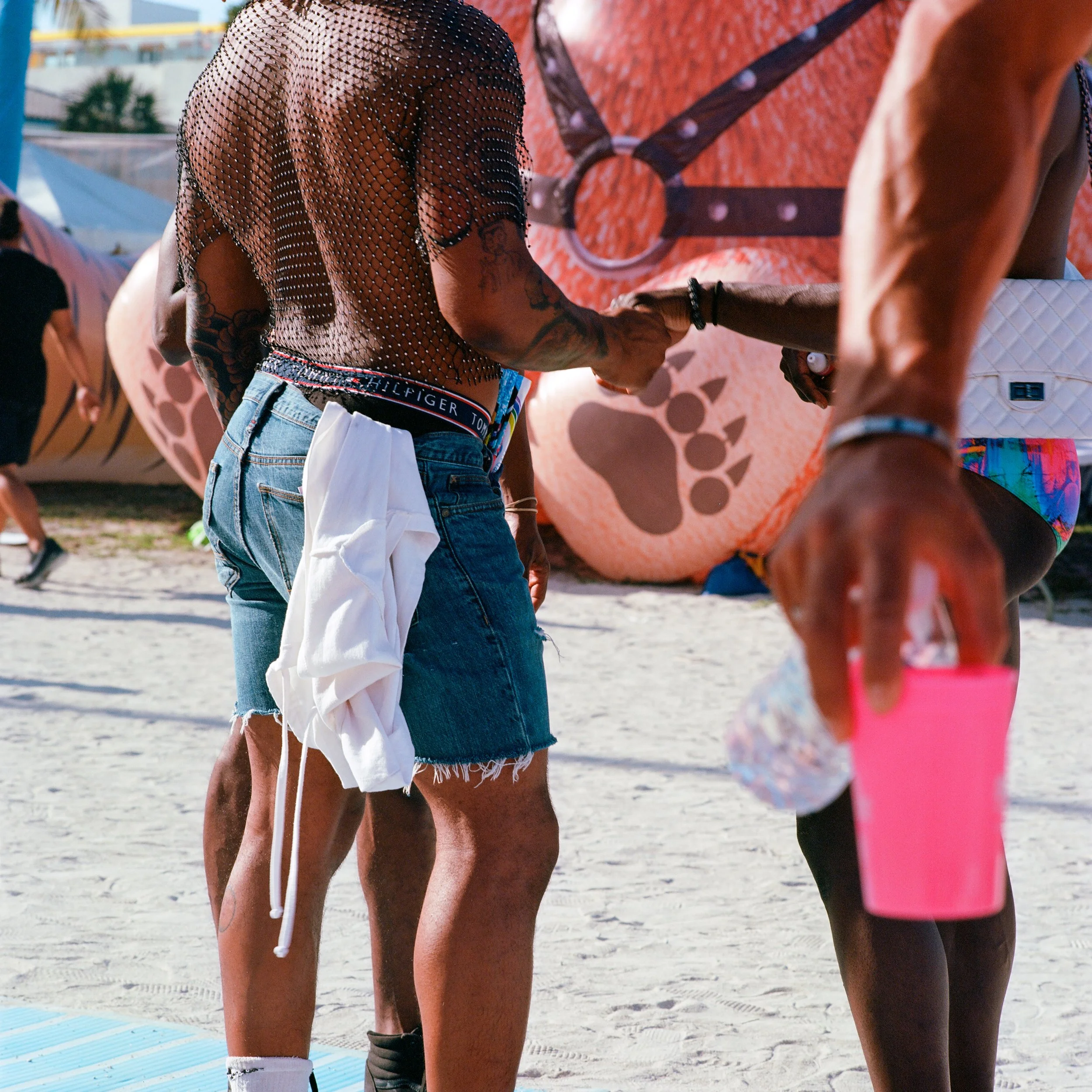 Two people handshake at a beach event, with large inflatable bear and others in background.
