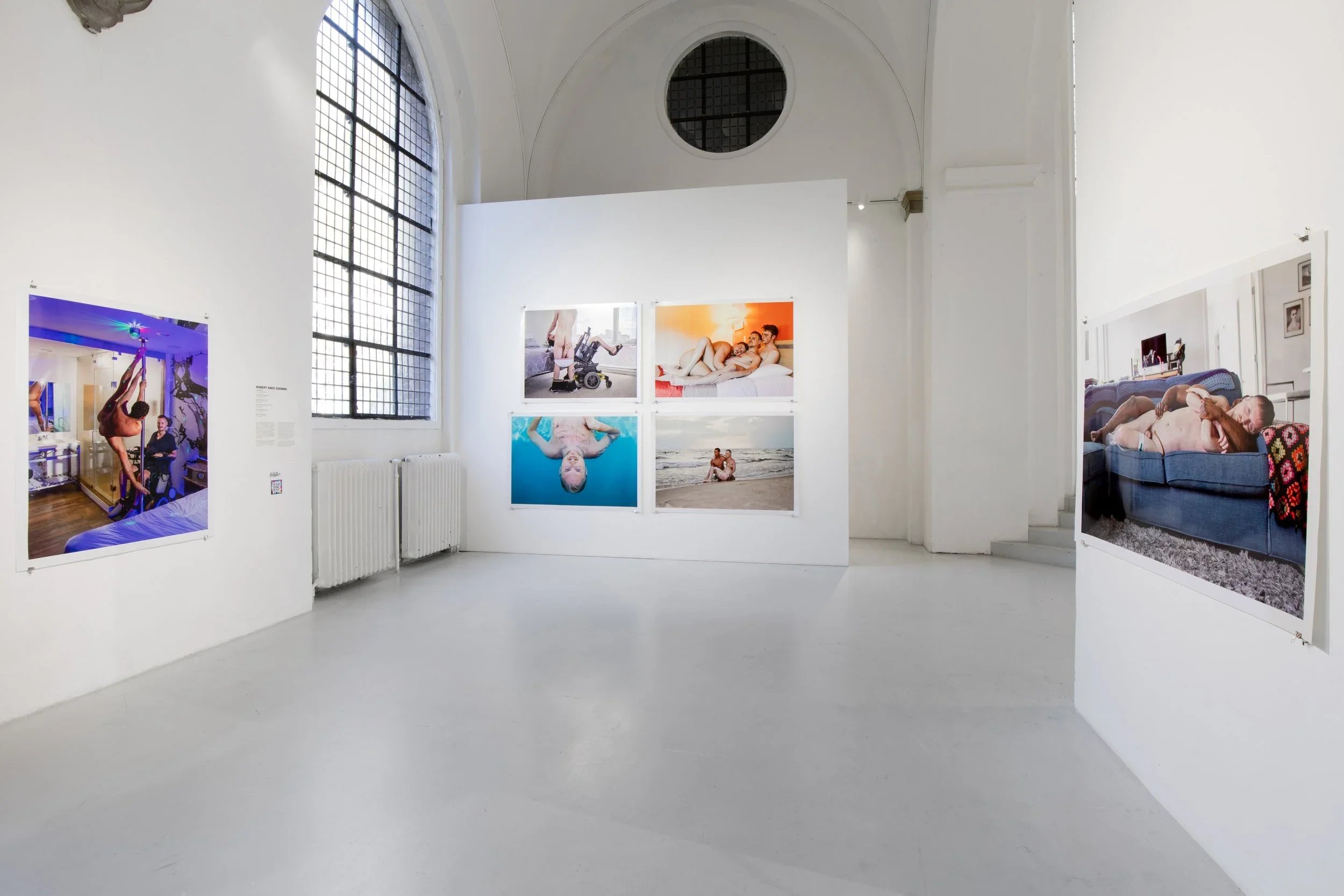 Art gallery with photographs on white walls, large window with grid panes, and a clean, minimal interior.