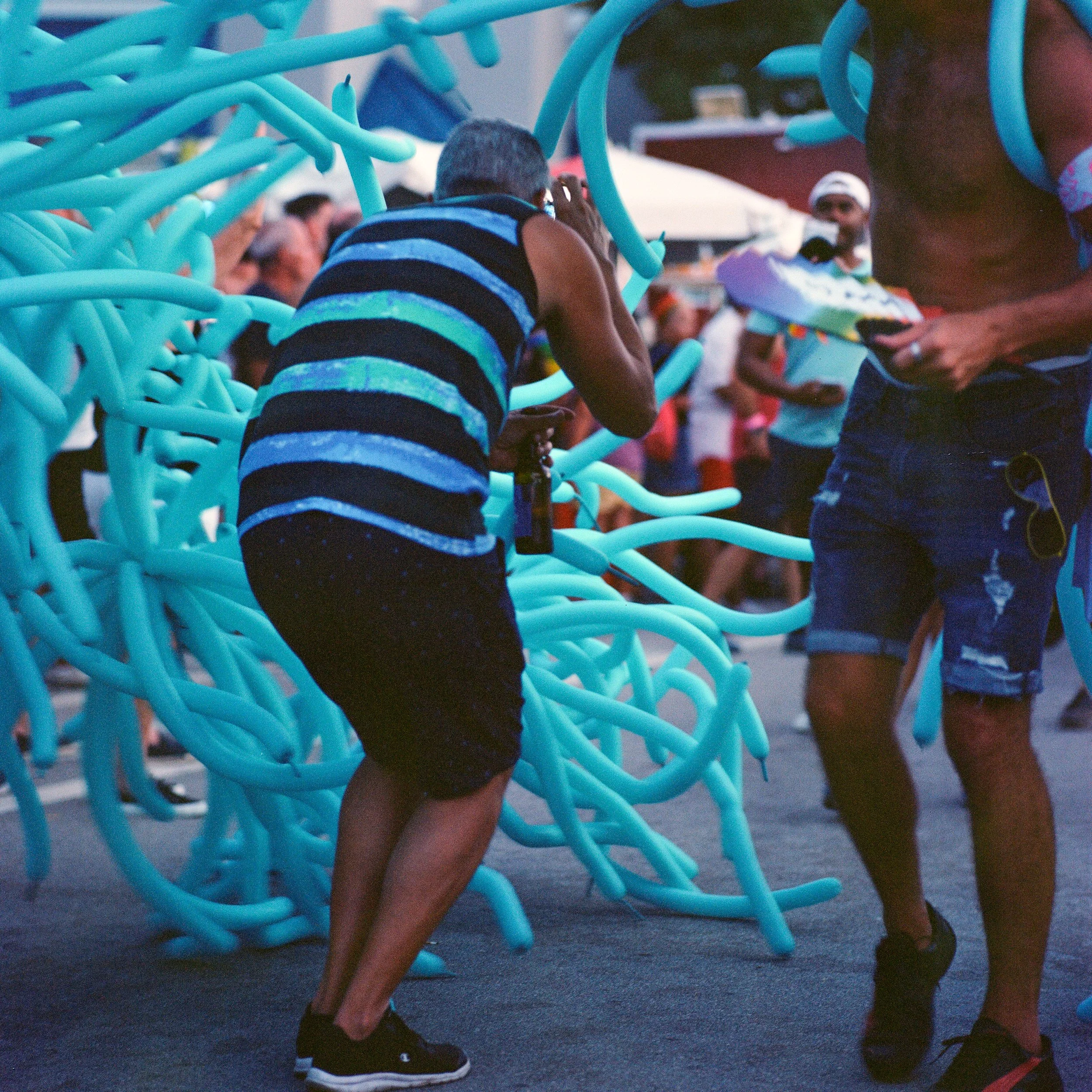 Person crouching among blue balloon sculptures during a crowded outdoor event.